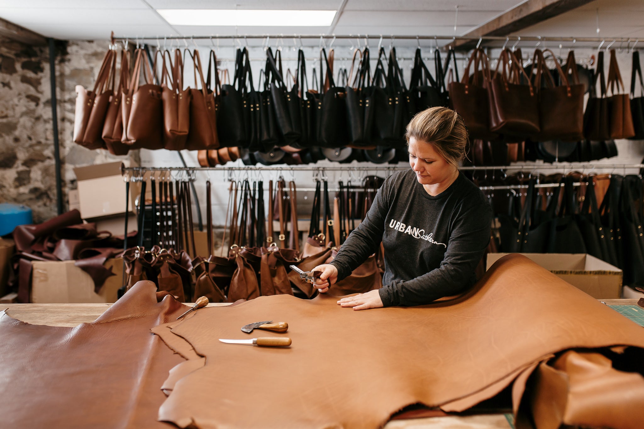 A woman begins cutting a leather hide, in preparation of crafting a new handbag.