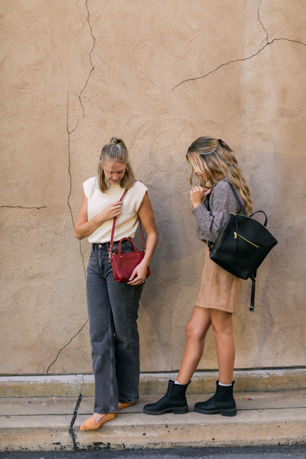 A woman carries a Cassidy Crossbody in Merlot while standing next to a woman carrying the Urban Southern Brooklyn Backpack in Black.
