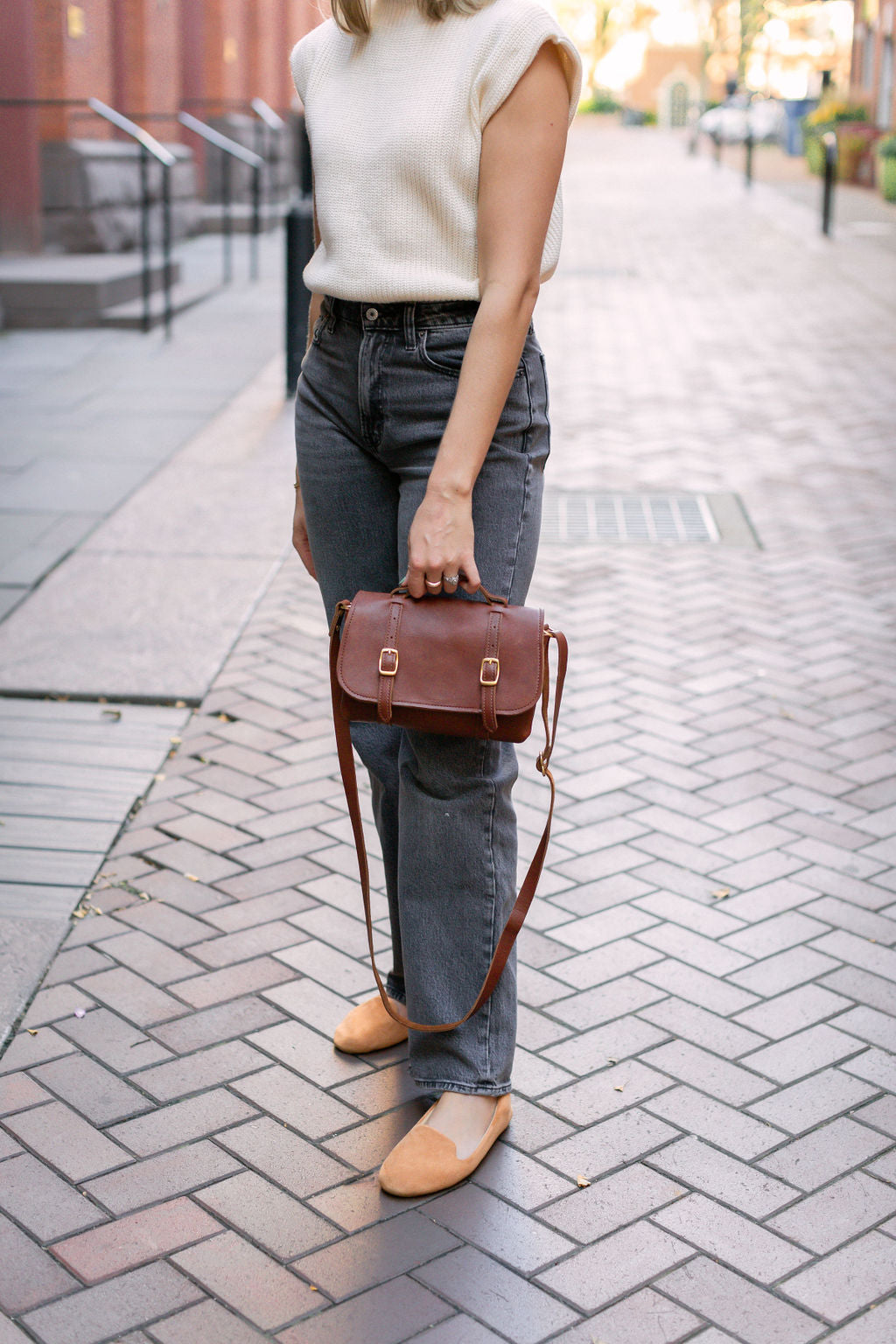 Woman holds Carriage Crossbody Bag in Cognac by top leather handle