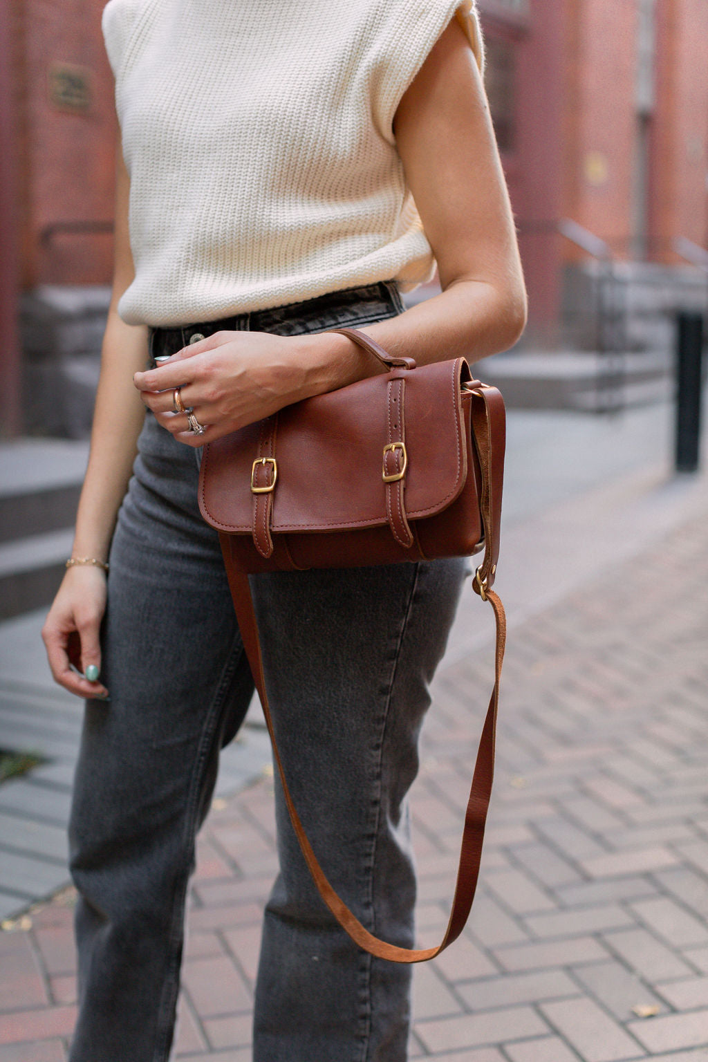 Woman carries the Carriage Crossbody on her wrist using the top leather handle.
