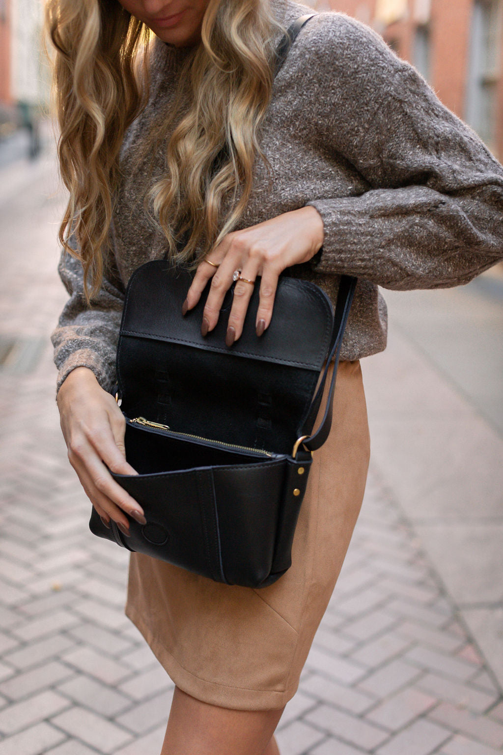 Woman opening the Carriage Crossbody while wearing it over her shoulder