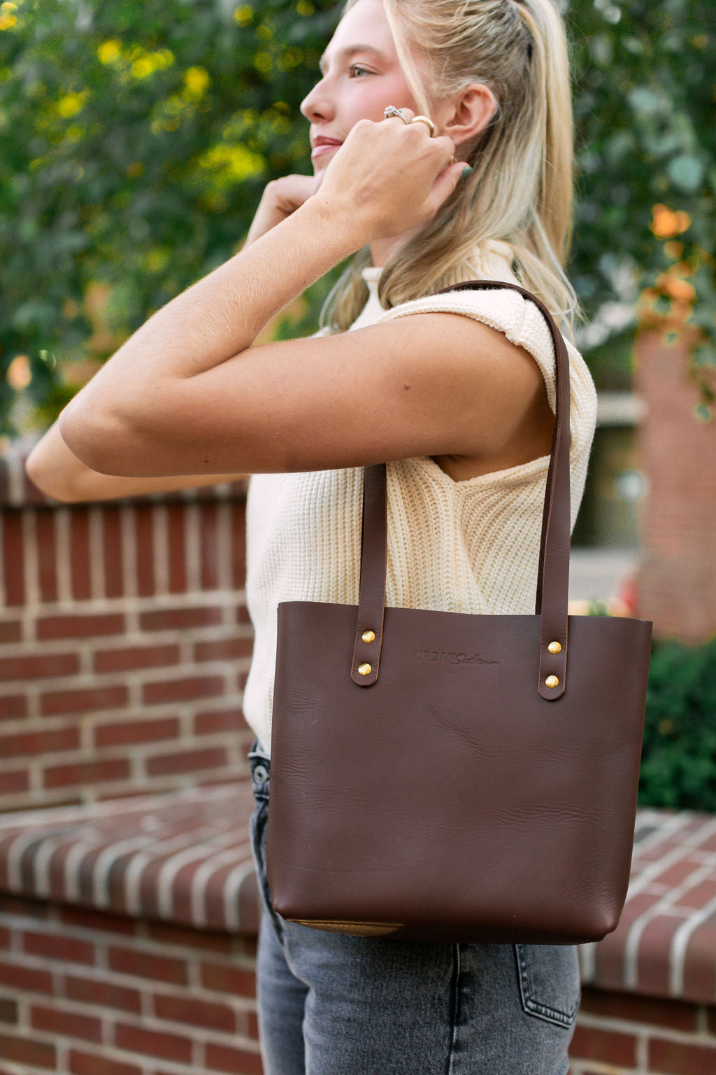 A woman carries the Mini Urban Tote in chestnut on her shoulder.