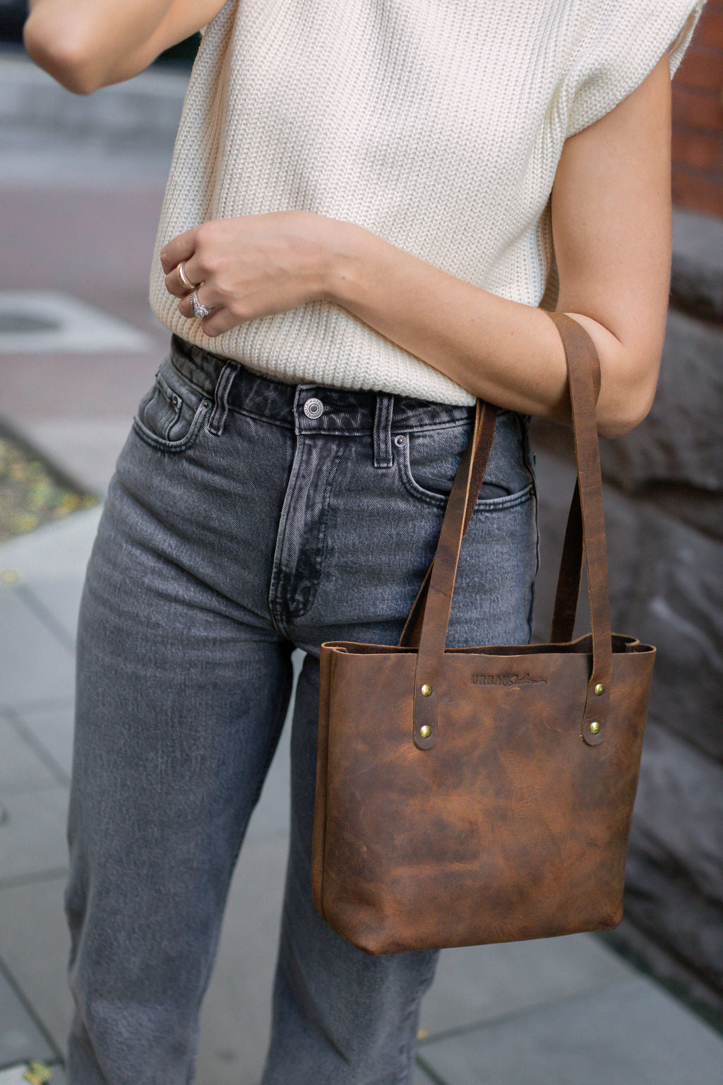 A woman carries the Mini Urban Tote in Rustic Brown on her arm.