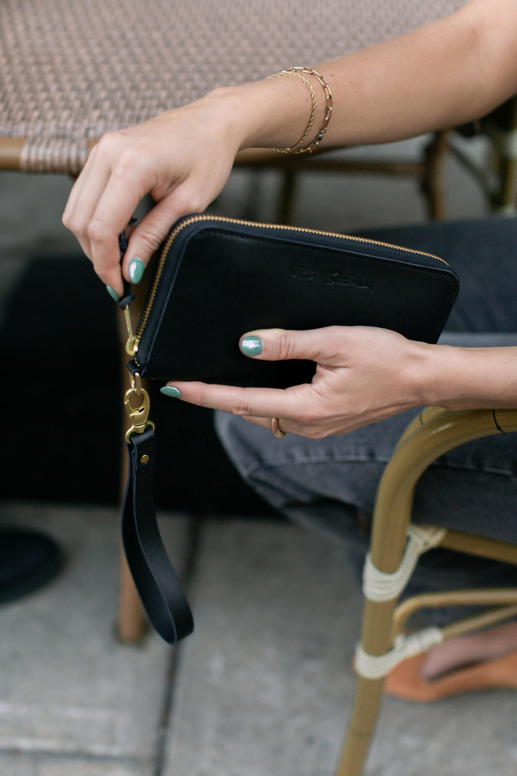 A woman sitting at an outdoor coffee shop holds and unzips a Black Urban Zipper Wallet.