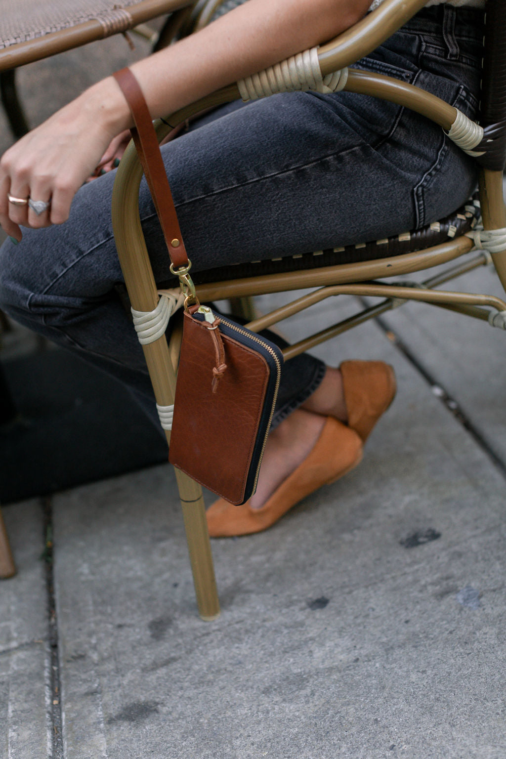 A woman sitting at an outdoor coffee shop holds a cognac Zipper Wallet on her wrist.