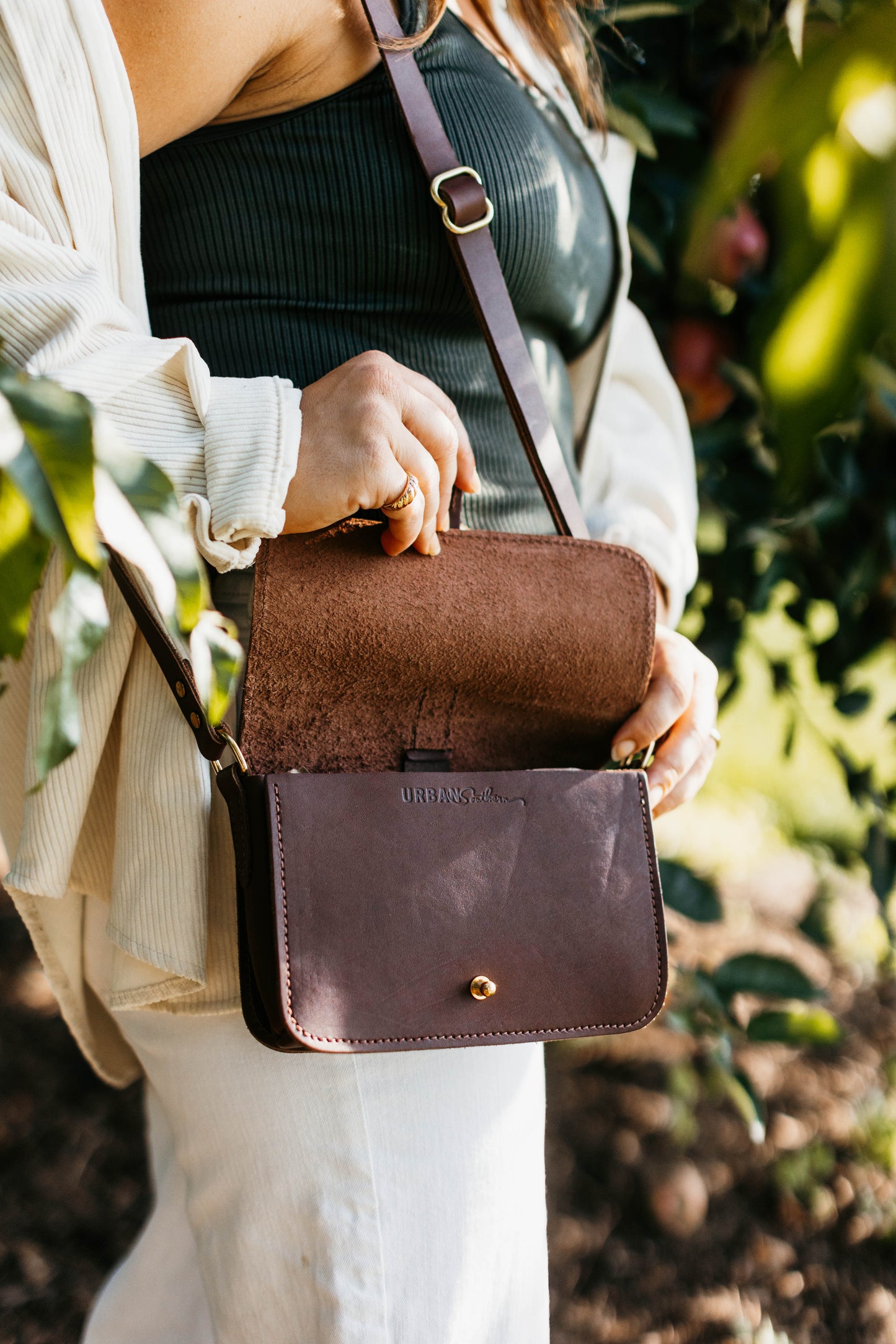 A woman opens the 5-Pocket Crossbody Bag, revealing the leather underside of the front flap.