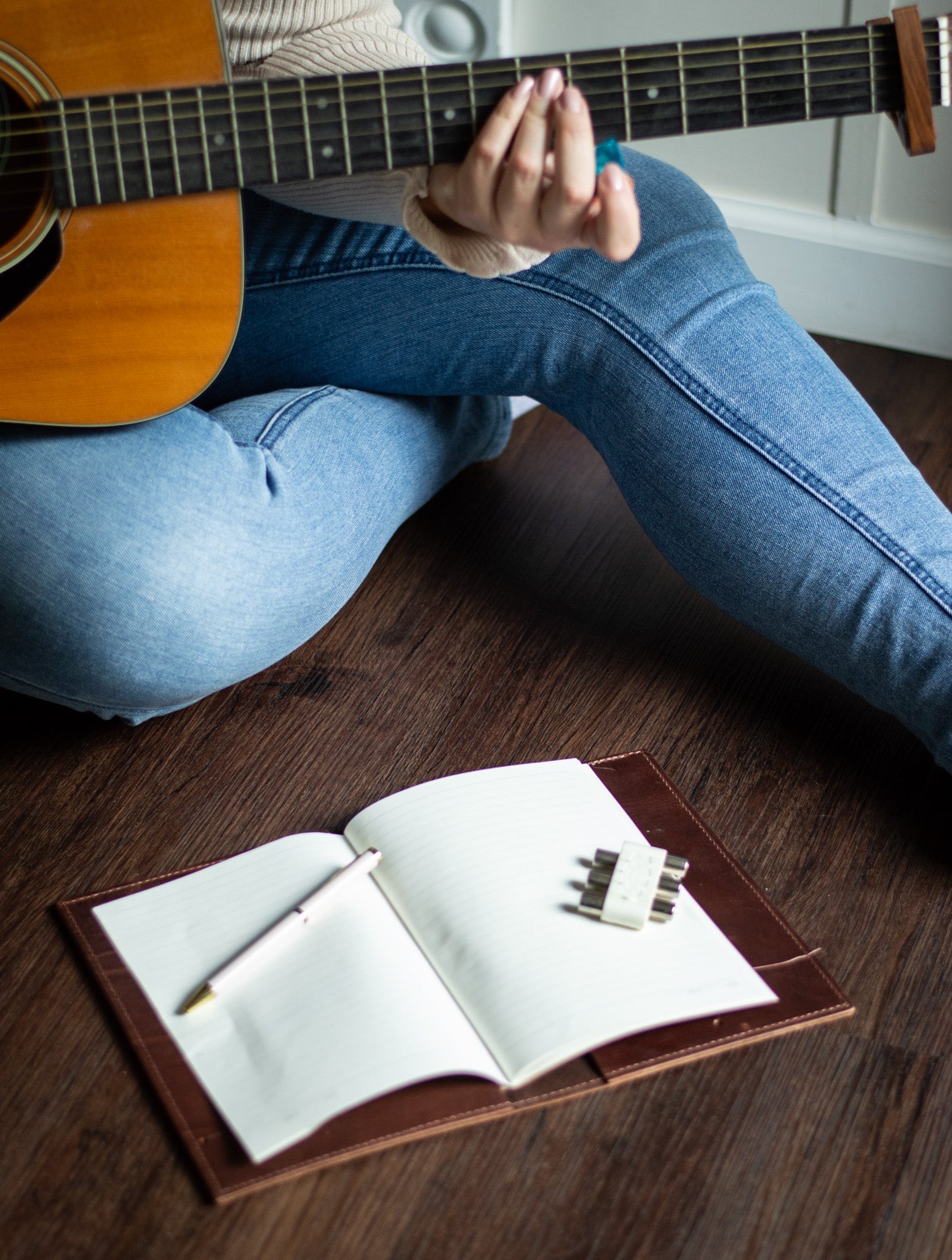 A unique leather A5 Journal lays open on the floor, next to a woman playing a guitar.