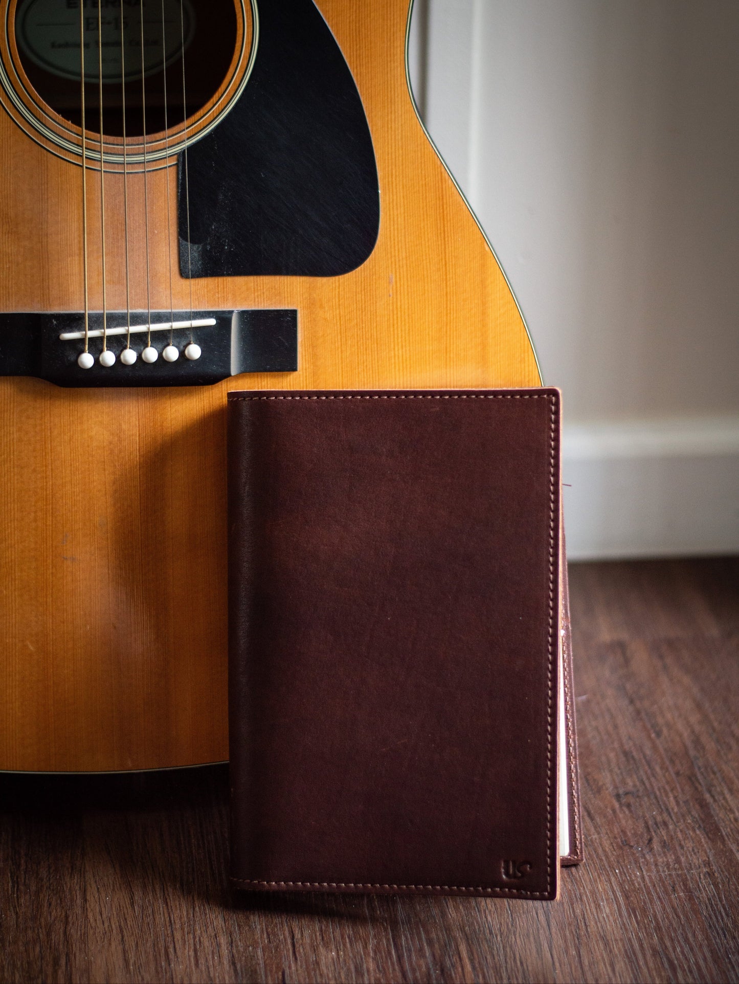 A beautiful leather A5 Journal, sits on the floor next to a guitar.