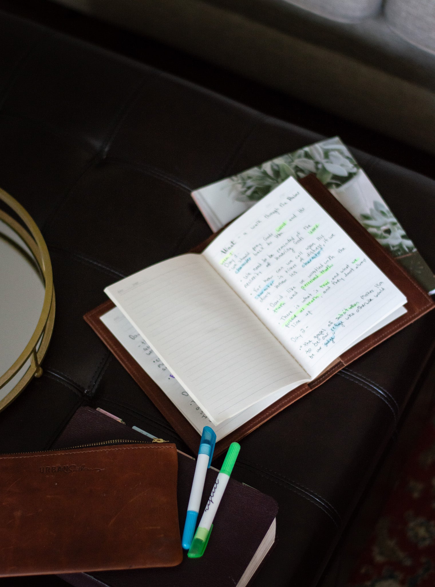 On a coffee table, an array of pens & devotionals are laying out, alongside an open A5 Journal full of handwritten notes.