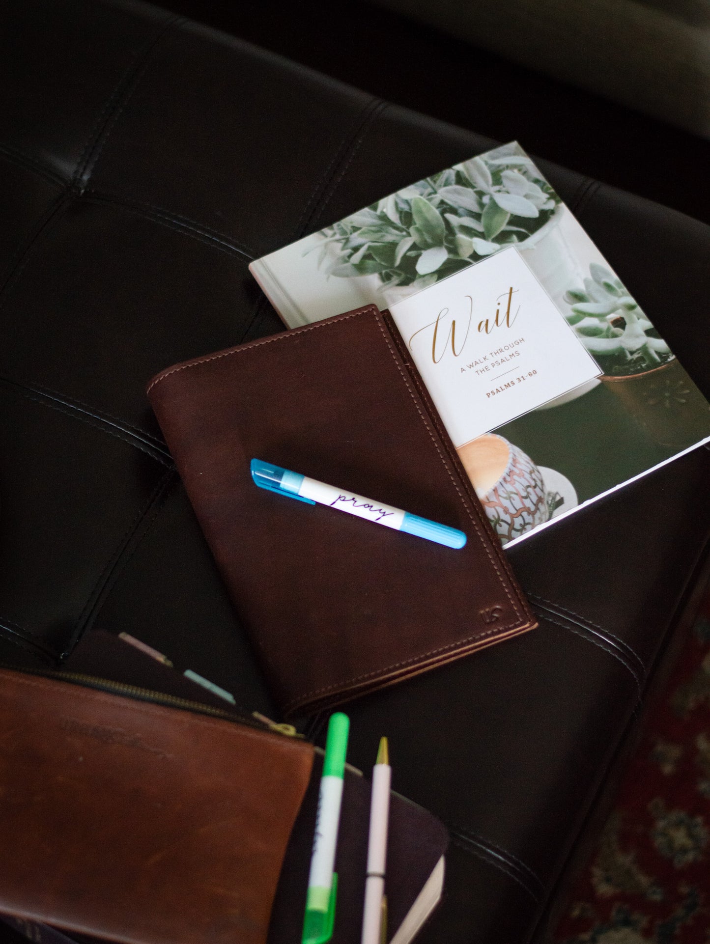 On a coffee table, a full-grain leather A5 Journal lays next to a devotional notebook & a selection of pens.