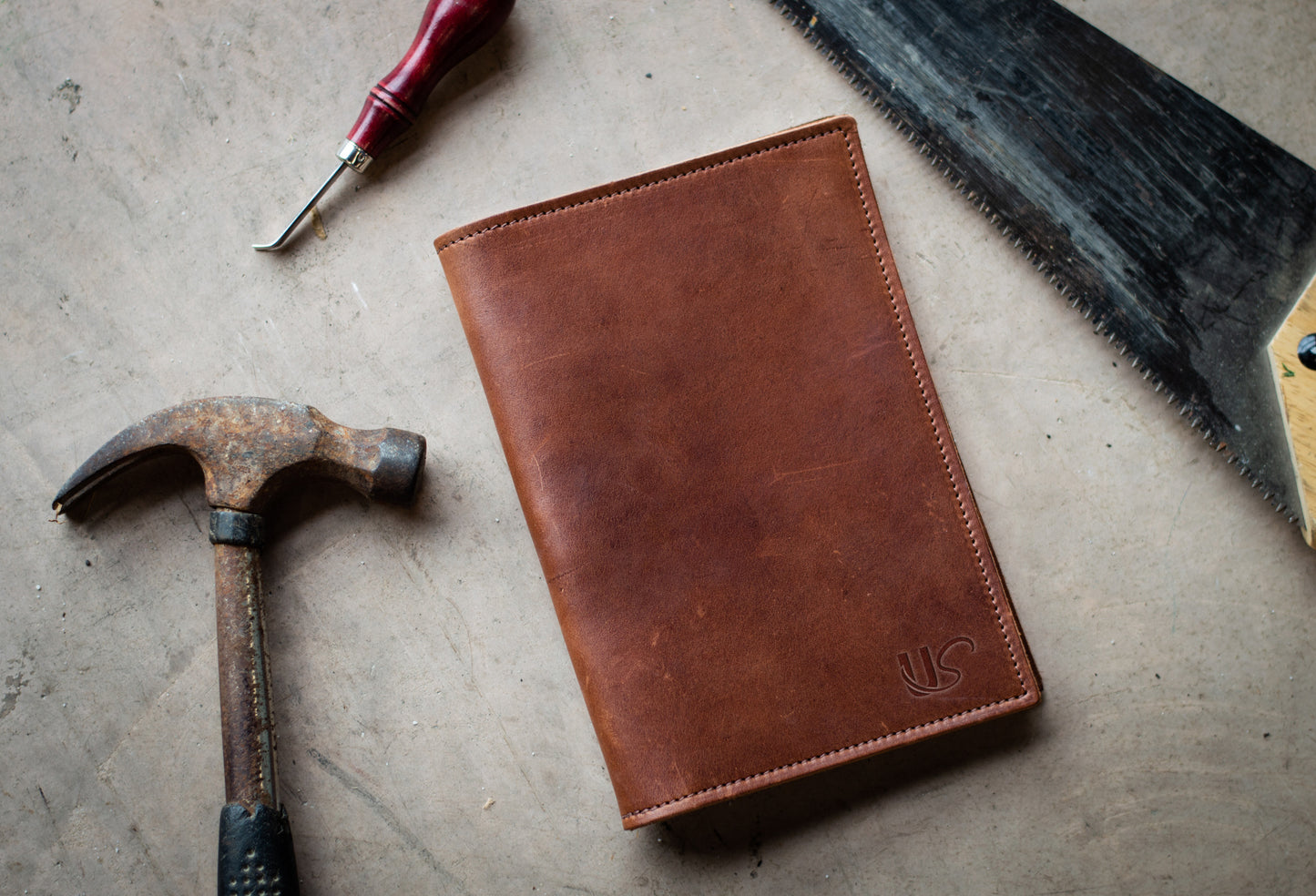 An A5 leather Journal is lying next to an assortment of tools on a workshop floor.