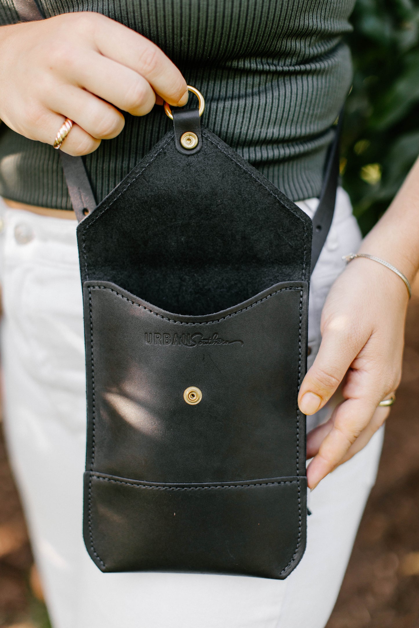 A woman opens the lid of a Postal Crossbody, revealing the Urban Southern logo hidden underneath the front flap.