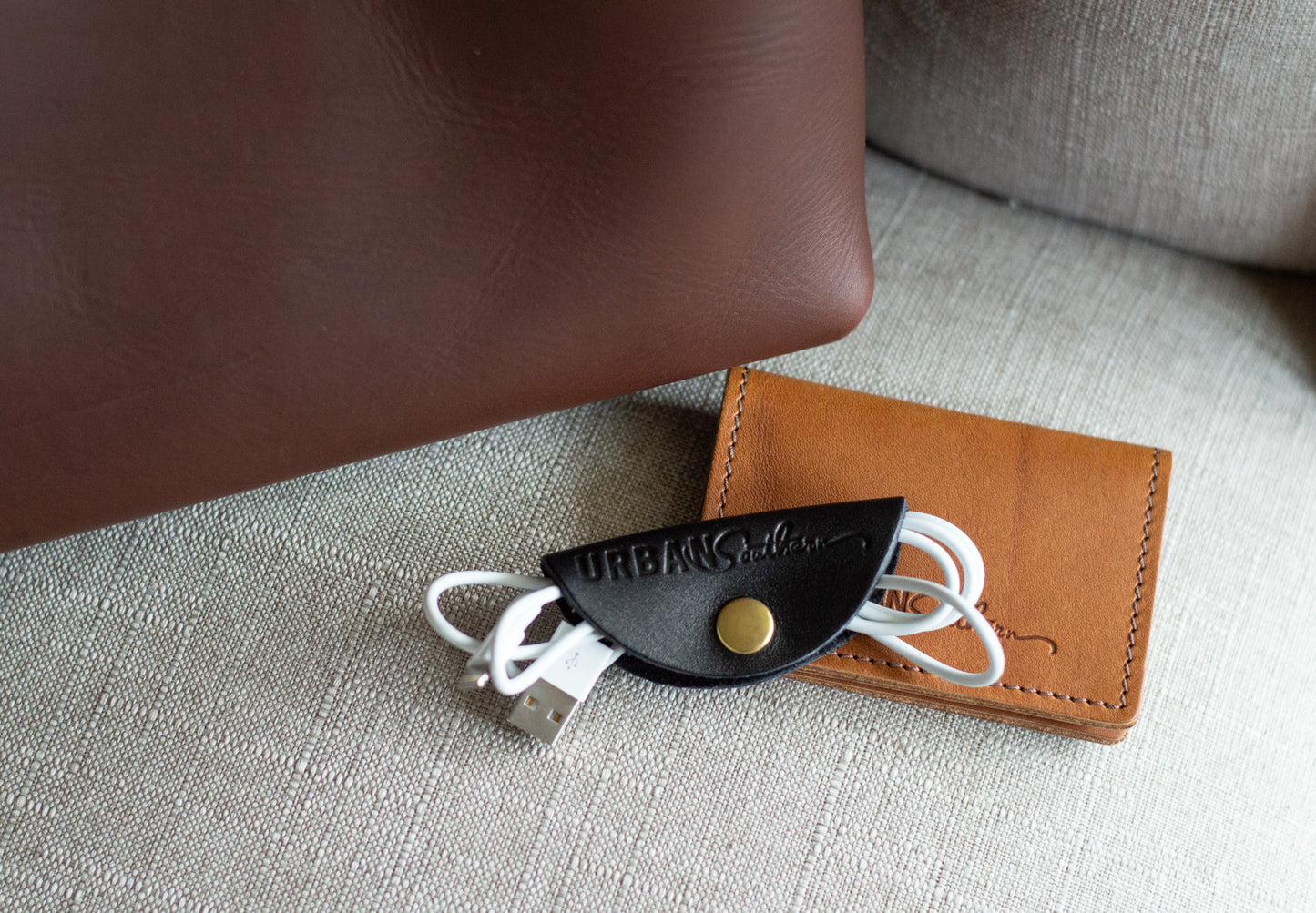 A black Urban Cord Wrap lays next to a honey Urban Card Wallet.