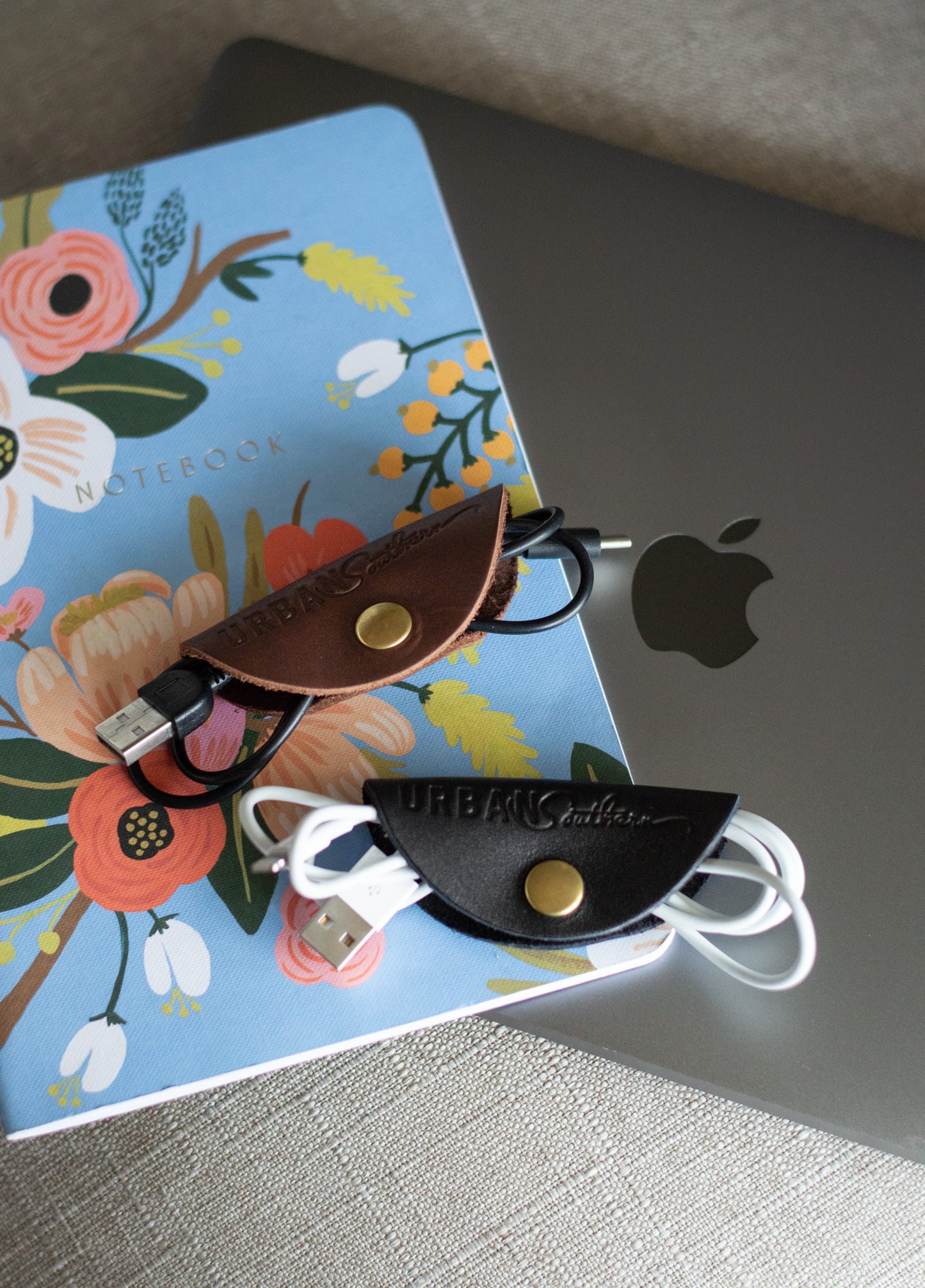 Two Urban Cord Wraps, one chestnut, one black, lay on top of a laptop & notebook.