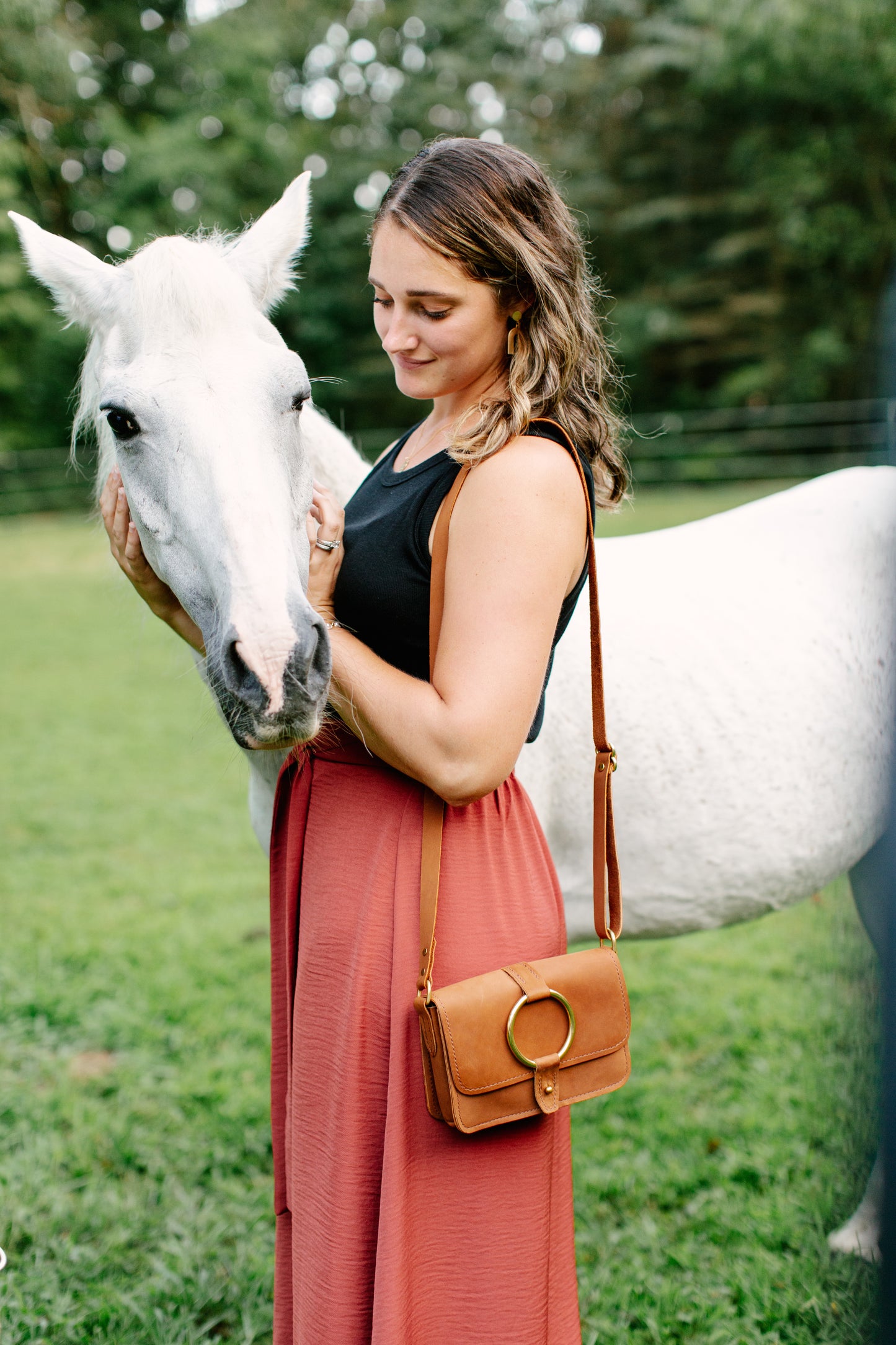 The 5-Pocket Crossbody Bag in Honey color hangs over the shoulder of a woman petting a horse.