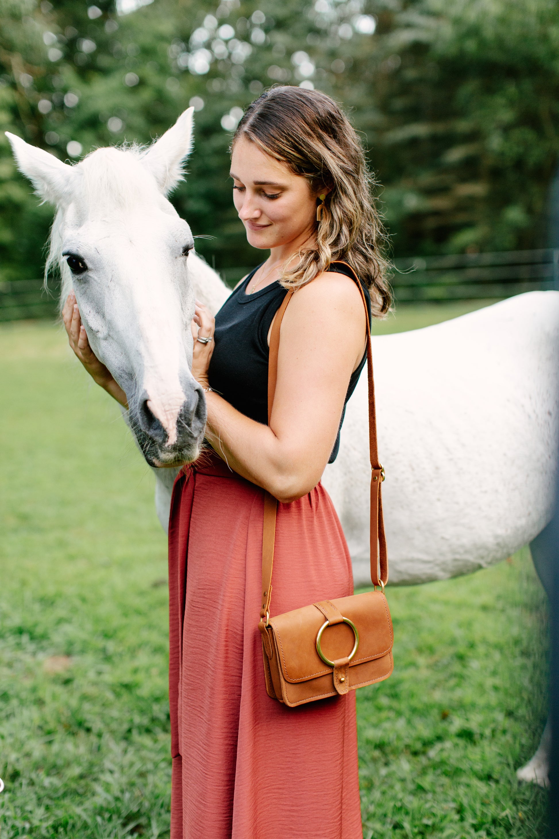 The 5-Pocket Crossbody Bag in Honey color hangs over the shoulder of a woman petting a horse.
