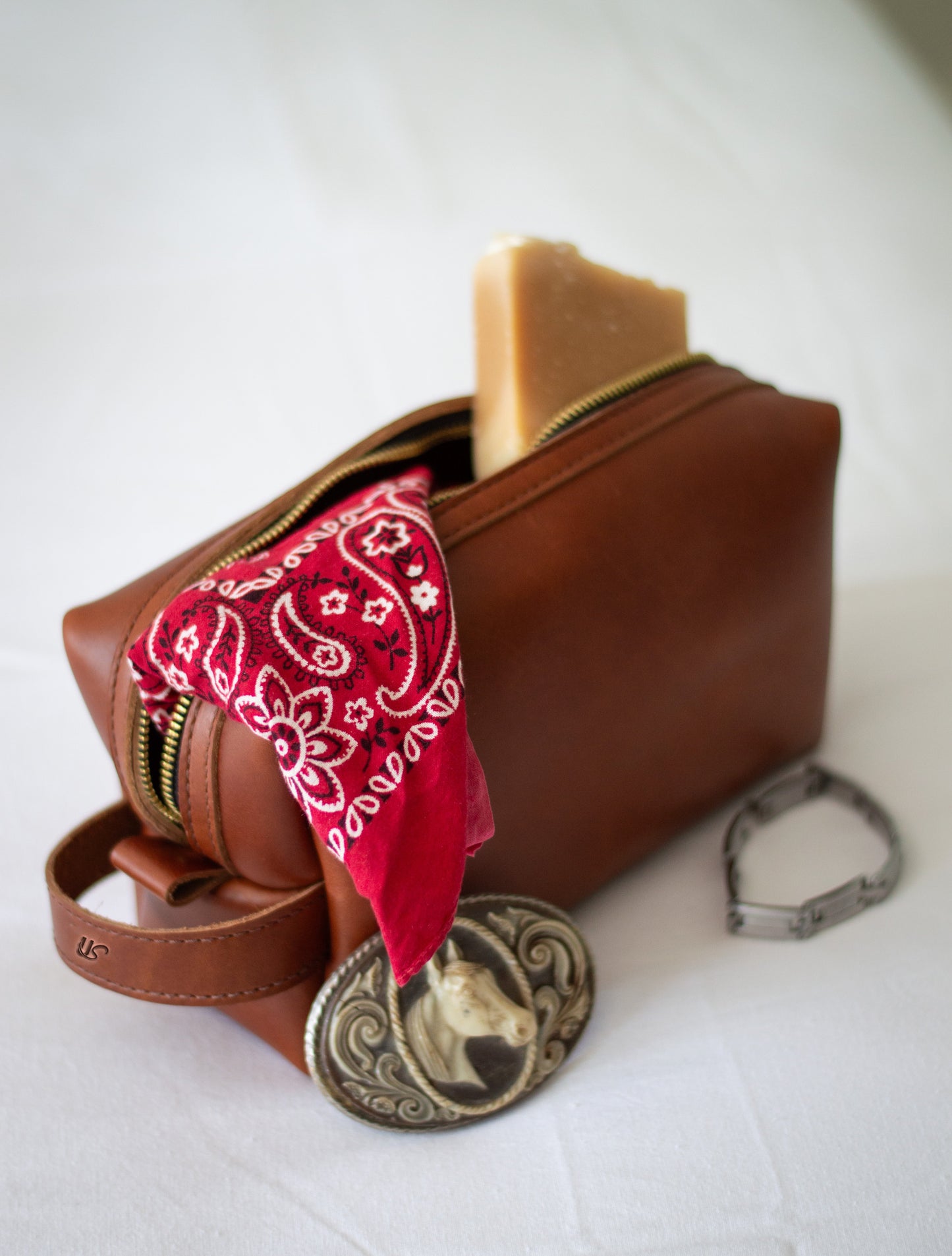 A bandana & bar of soap spill out of an open leather dopp kit.