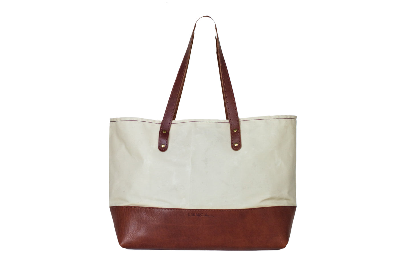 The Urban Southern handcrafted leather Large Canvas Tote features a Chestnut Brown leather bottom, two-handle strap, brass hardware, and engraved Urban Southern logo. Shown here in Cream.