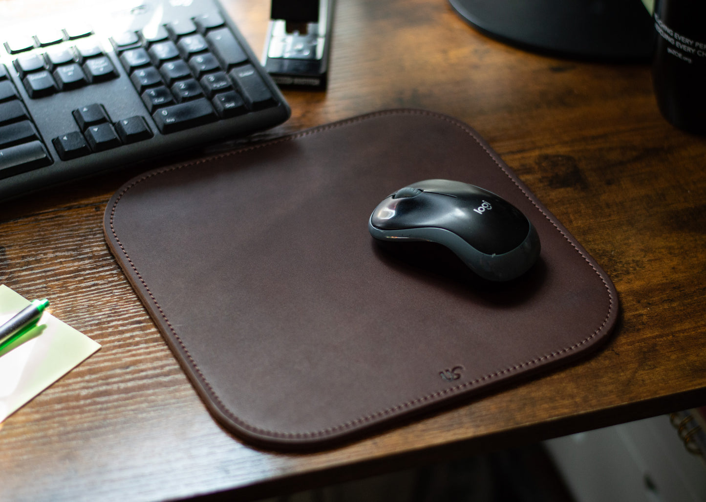A computer mouse sits on top of a full-grain leather Mouse Pad that is laying on a desk in an office.