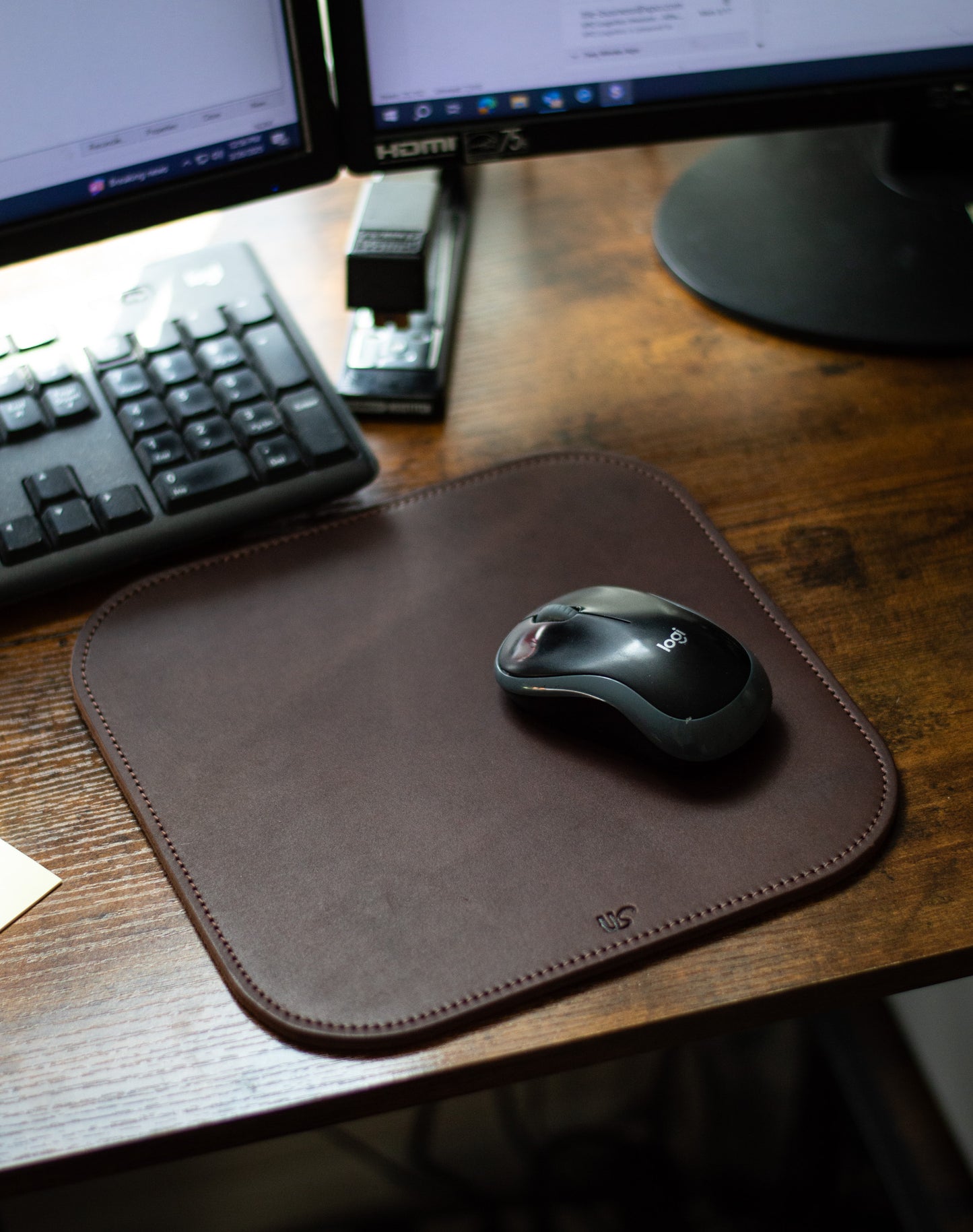 A computer mouse sits on top of a rich, full-grain leather Mouse Pad that is laying on a desk in an office.