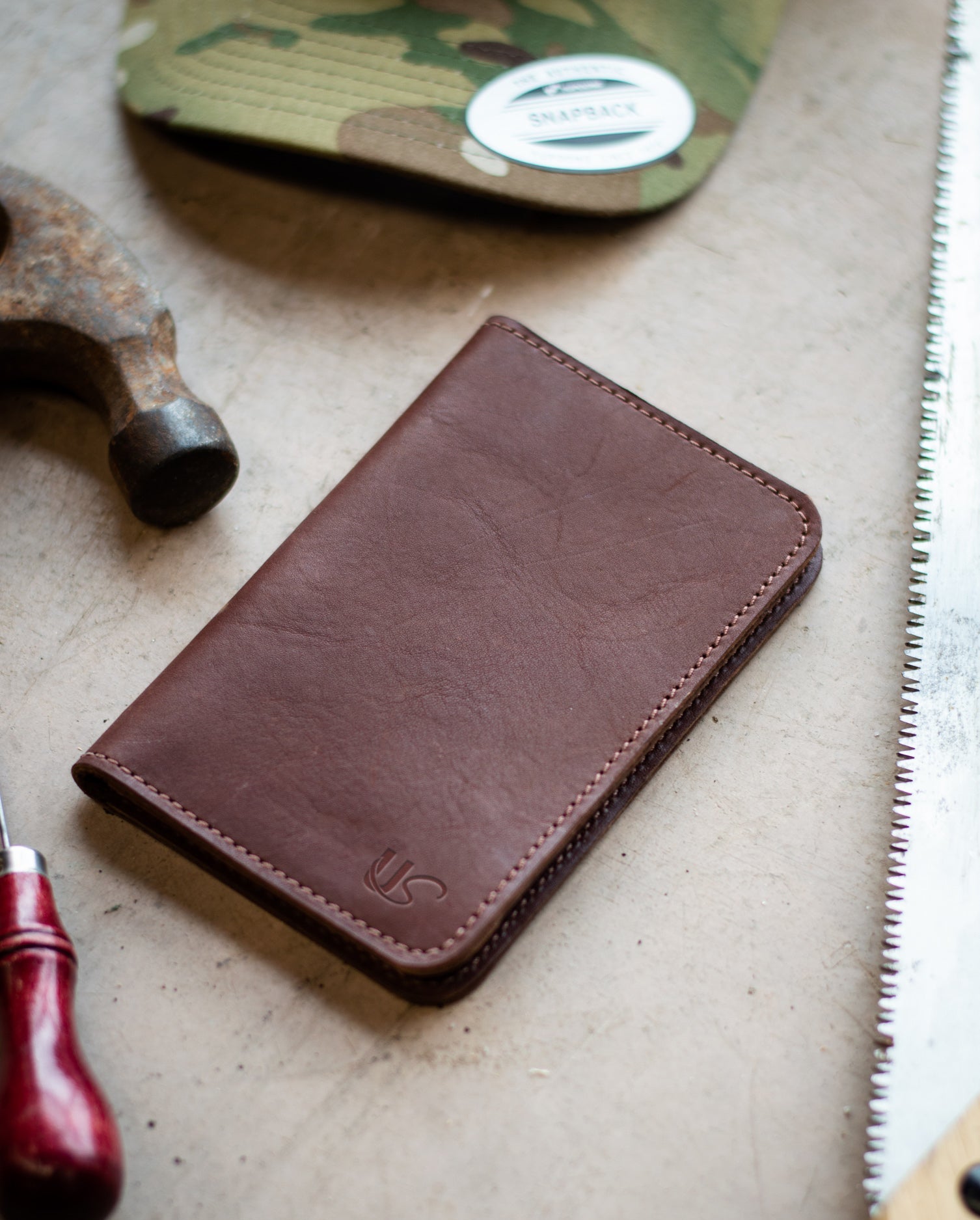 A leather Notebook Wallet, lays next to a collection of tools. Making any day on the job site more organized with it's 48 page memo book & business card slots