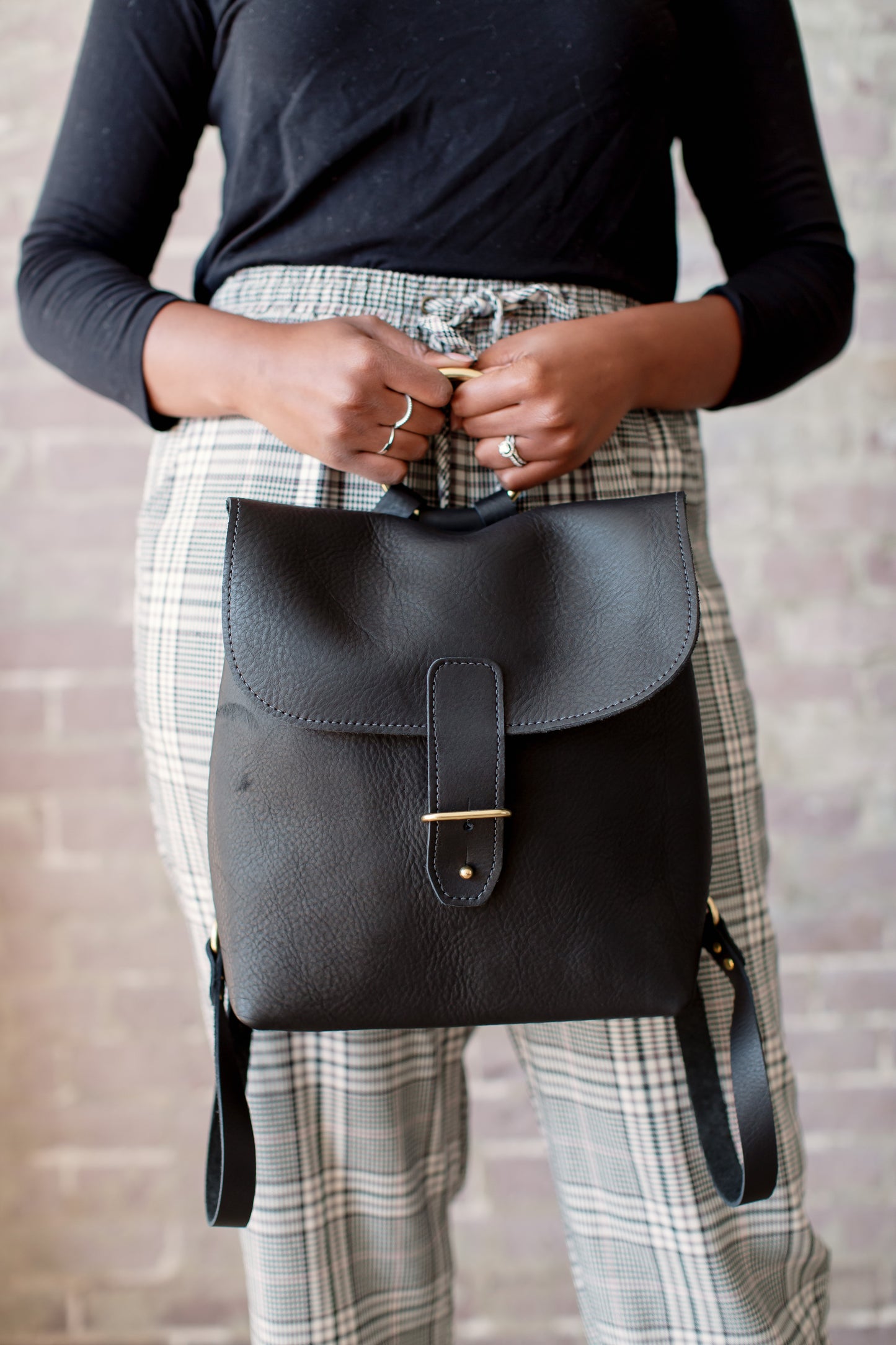 A woman holds the Monterey Backpack in her hands by the brass ring.