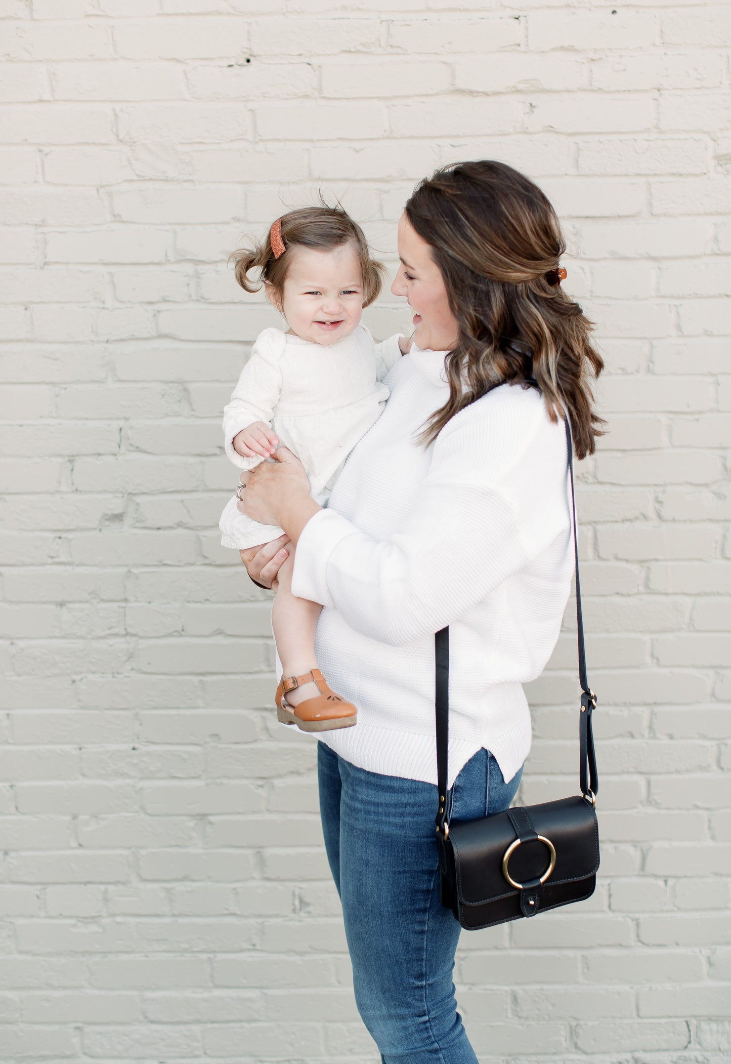 A woman holds a child while carrying the 5-pocket Crossbody Bag.