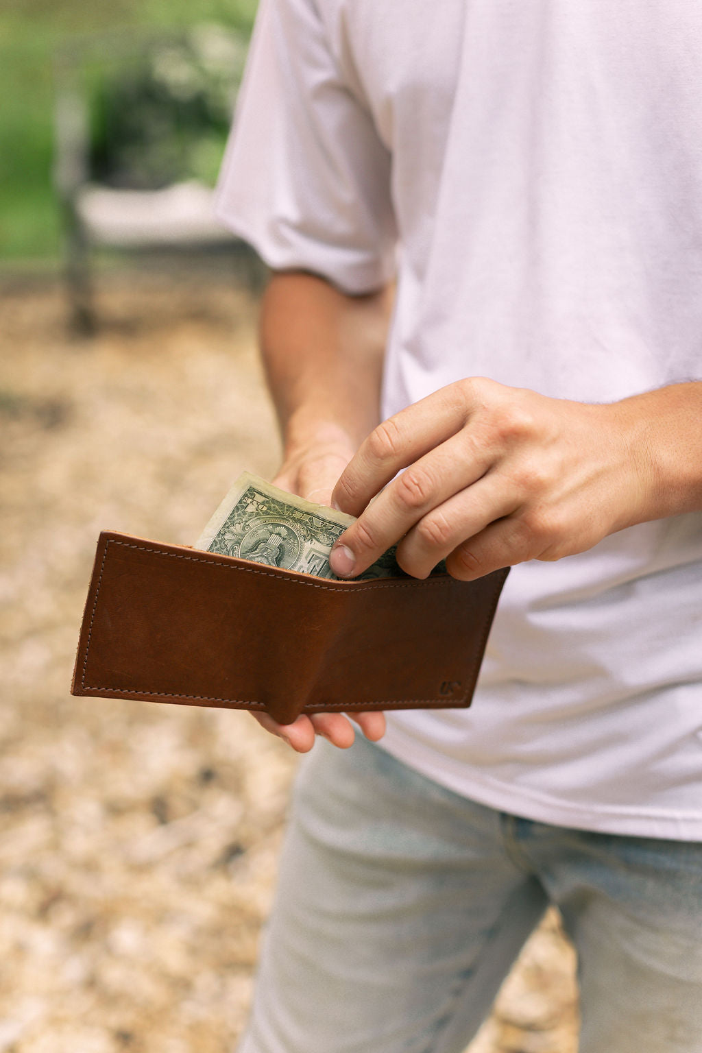 a man removes cash from his brown leather bifold wallet