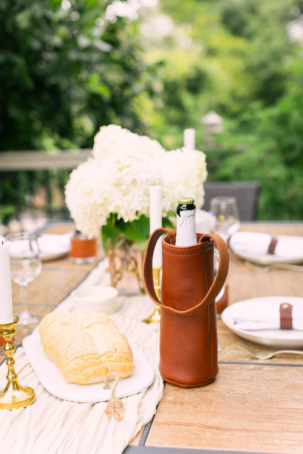Table setting with a leather wine holder, white flowers, and candles outdoors.