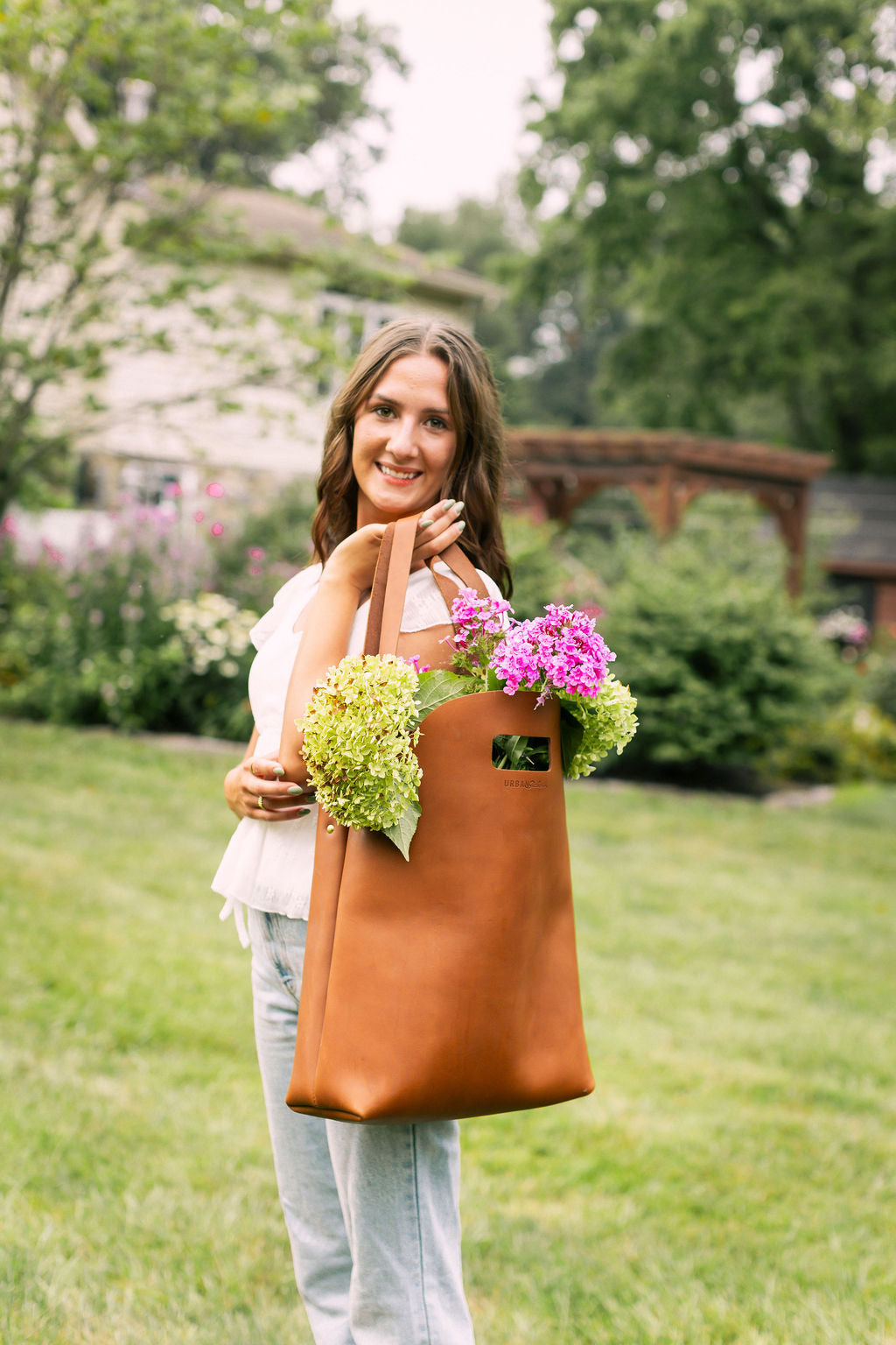 Woman holding a light brown leather tote with flowers in a garden setting