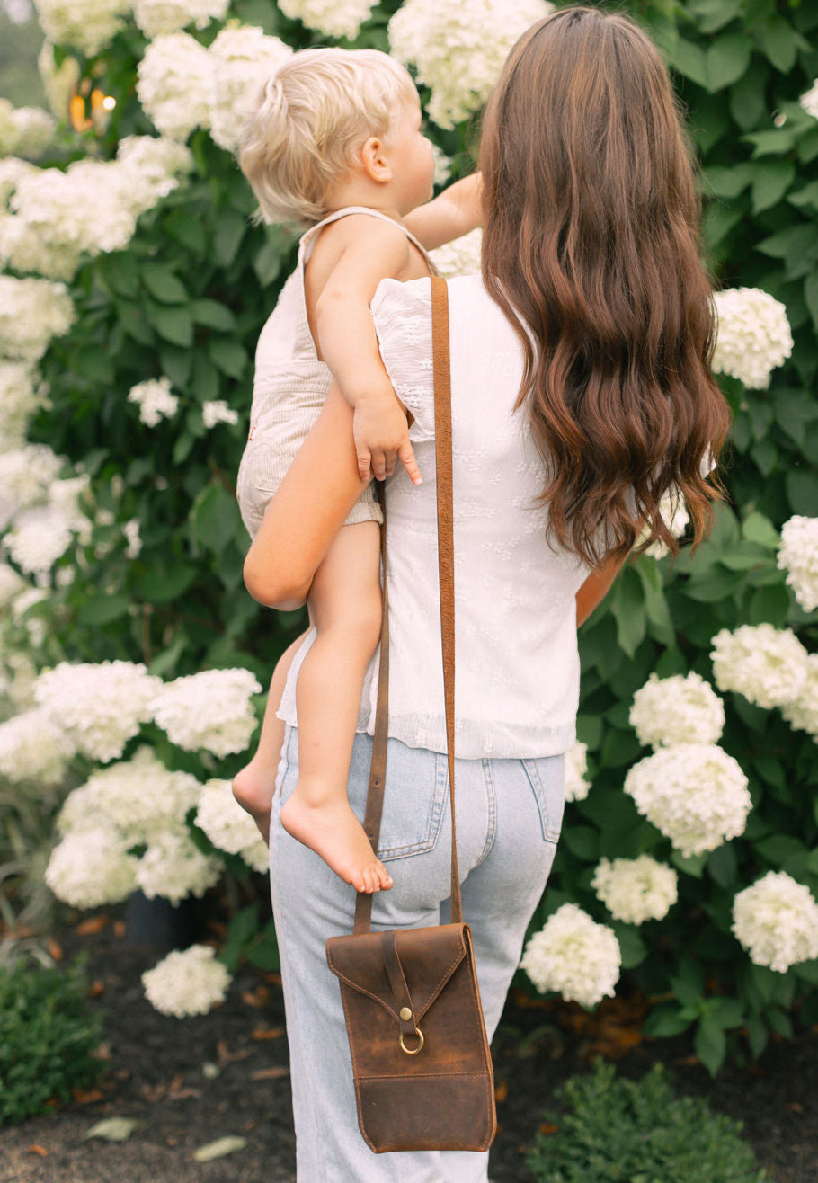 Woman holding a child with a brown leather bag in front of white flowers