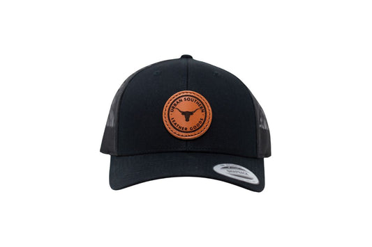A front view of a black leather patch hat, featuring the rustic longhorn Urban Southern logo on a circle leather patch.