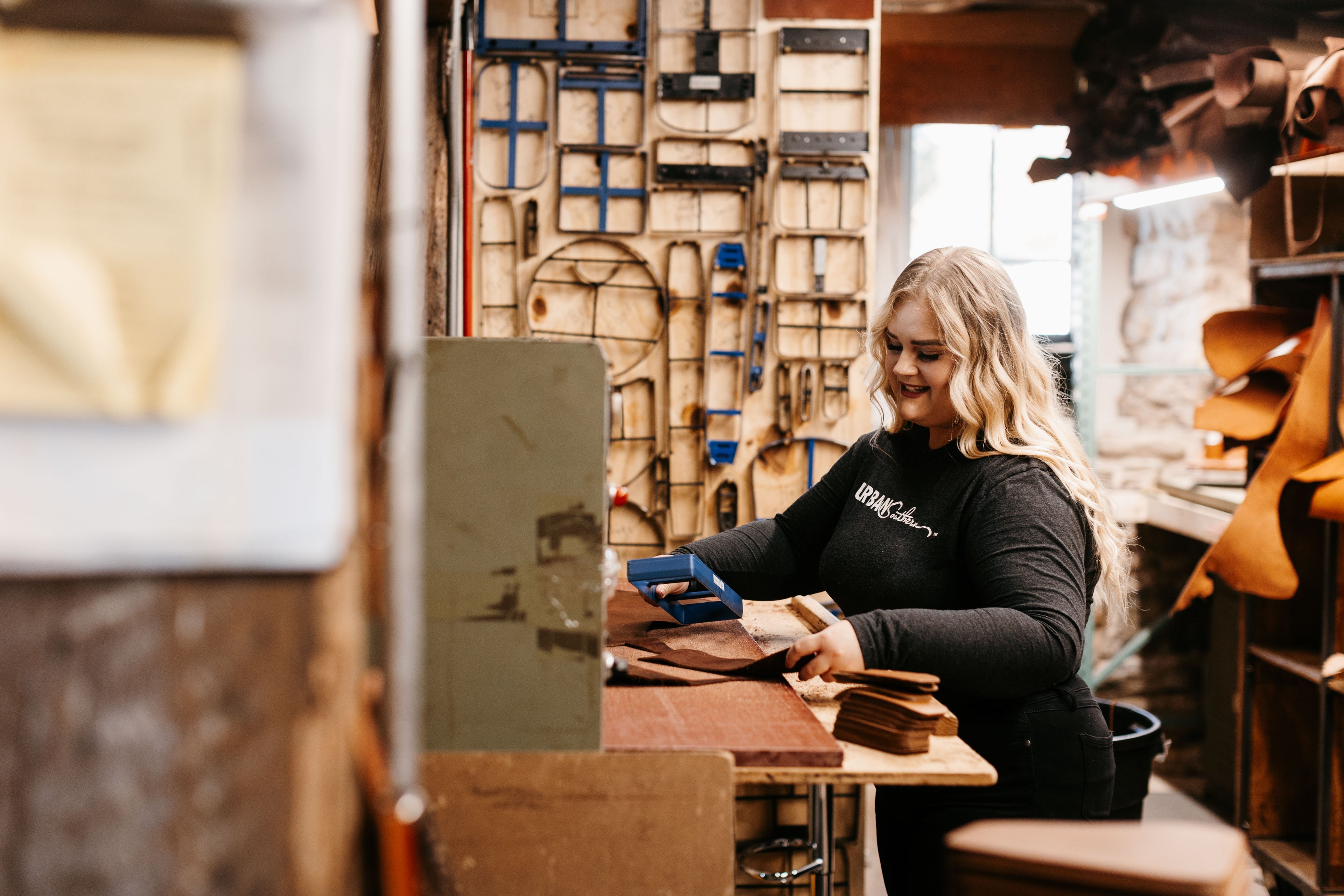 A woman stands in a workshop, cutting a leather hid into handbag pieces.