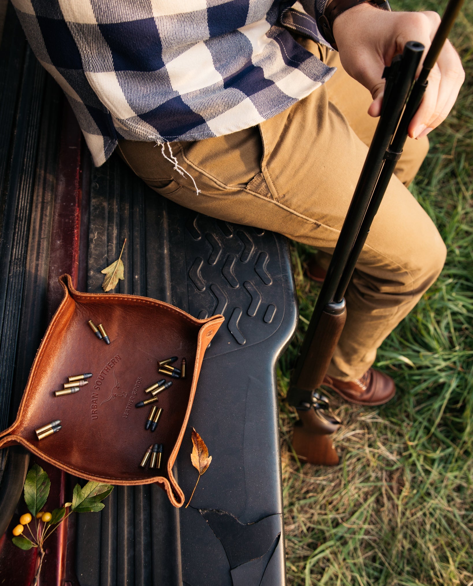 A leather valet tray filled with bullets, sits on the bed of a pickup truck, while a man loads a shotgun next to it.