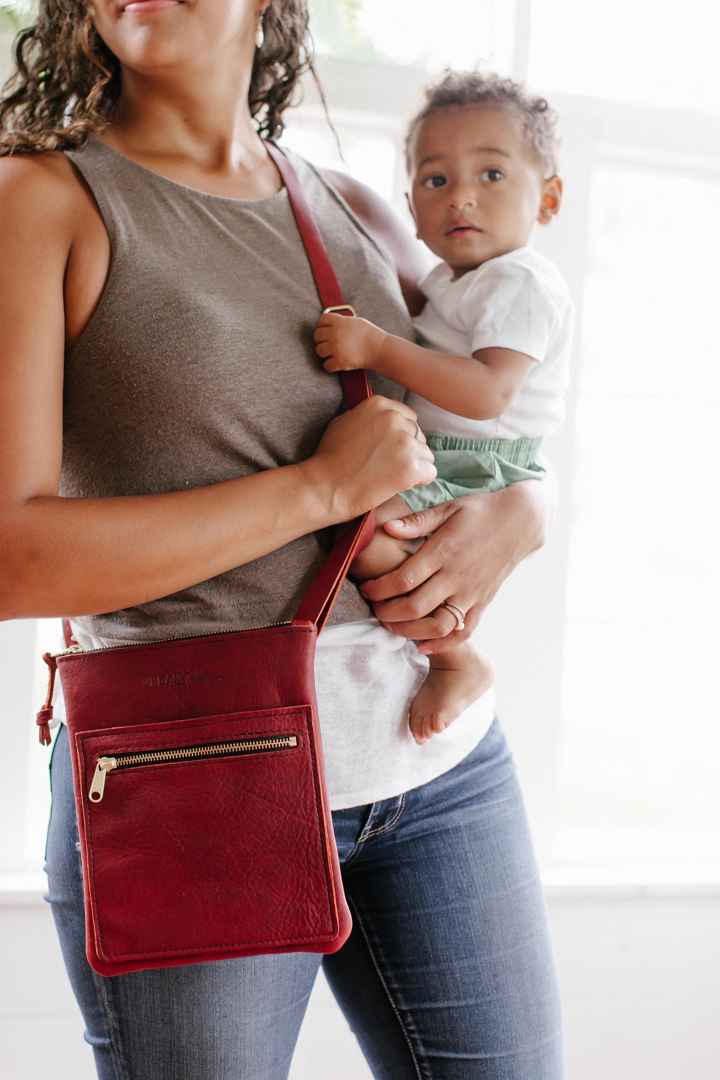 Woman holding a red slim crossbody bag and a child.