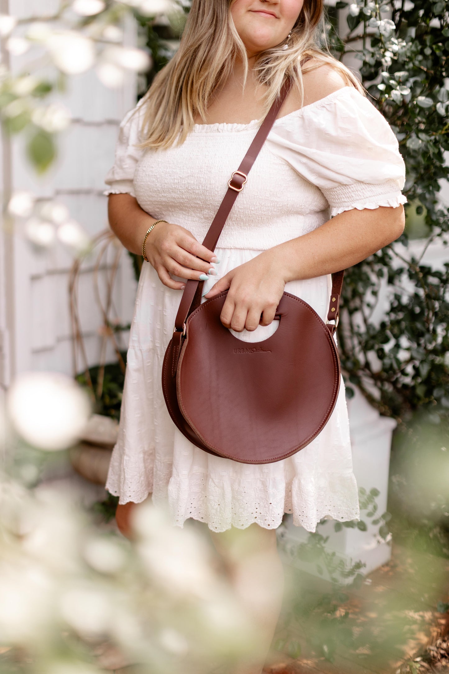 A woman holds the Britt Circle Crossbody in Chestnut Brown by its convenient grab handle.