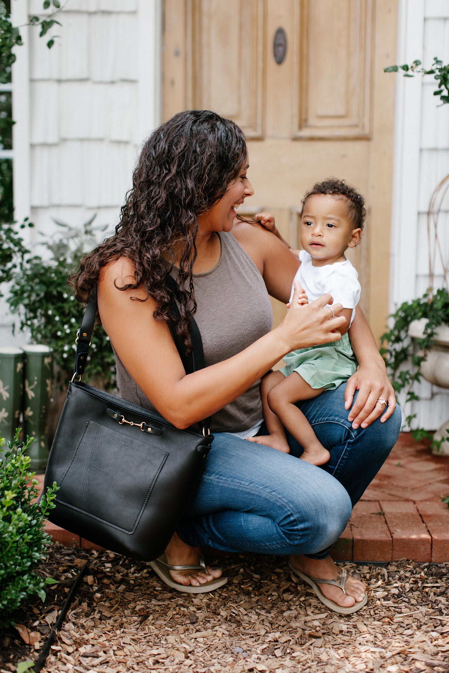 A woman holding a child in her arms, holds a black Lexington Julep on her shoulder.