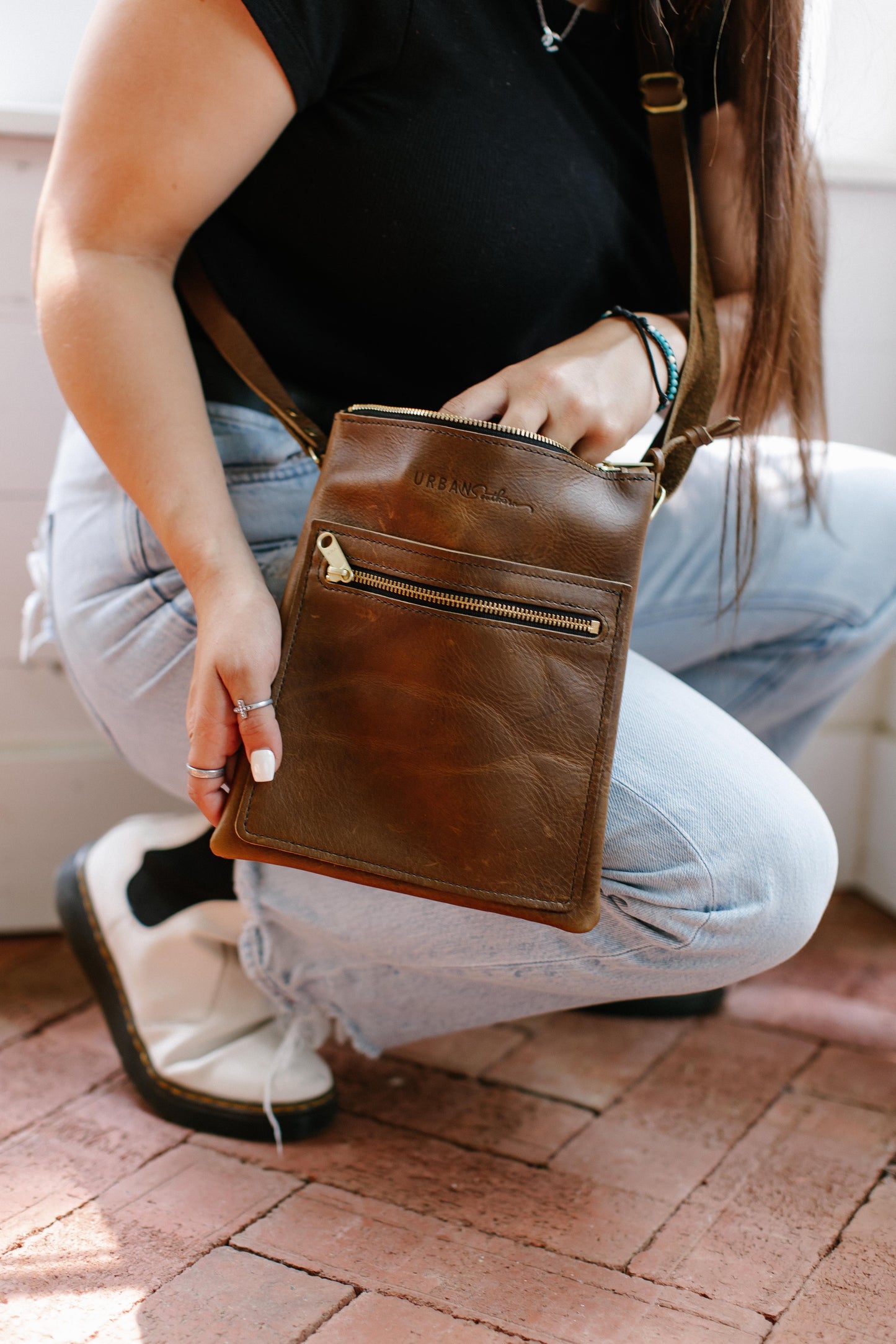 A woman reaches her hand into a mocha Urban Slim Crossbody.
