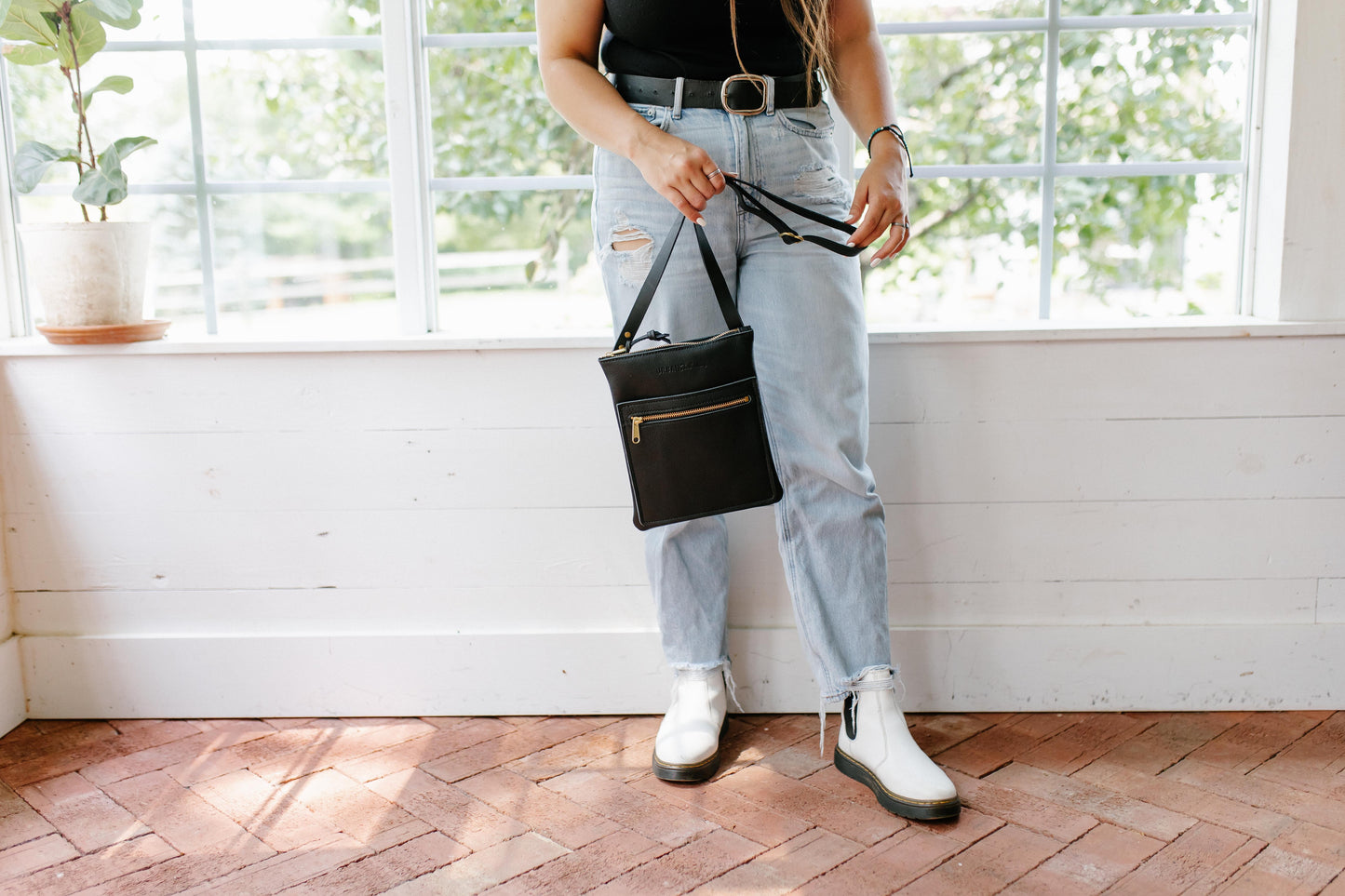 A woman holds a black Urban Slim Crossbody by its shoulder strap.