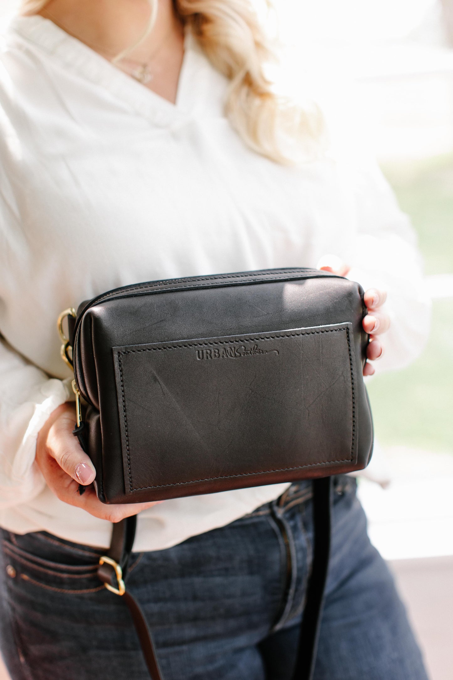 A woman holds the black Urban Sling in her hands, showcasing the front exterior pocket.