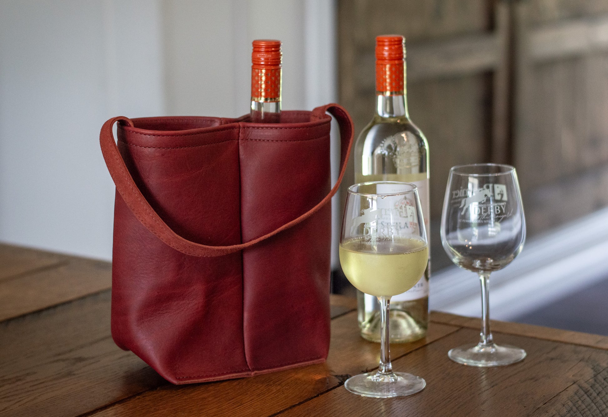On a table sits the merlot Double Wine Tote, alongside two wine glasses & a bottle of white wine.