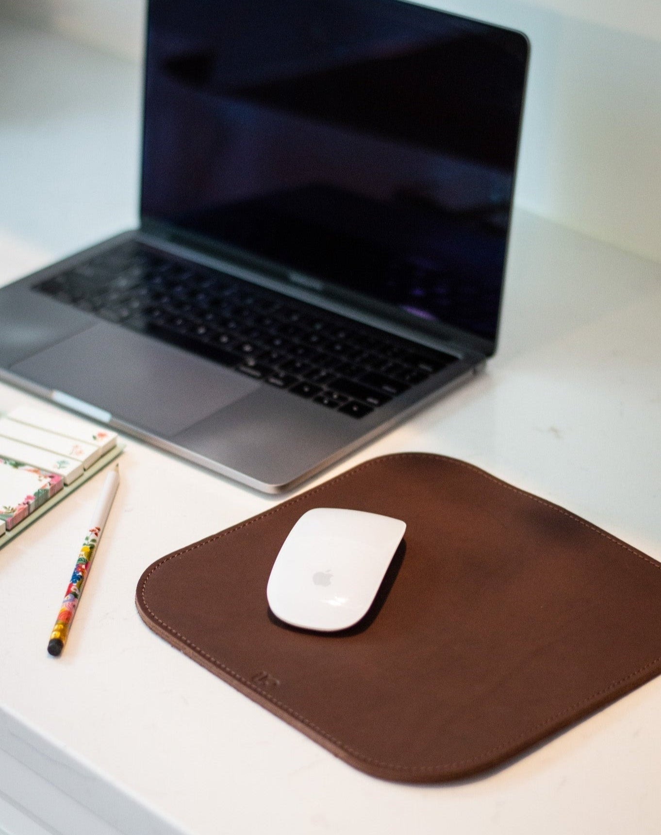 Laptop on a desk with a brown leather mouse pad and white mouse