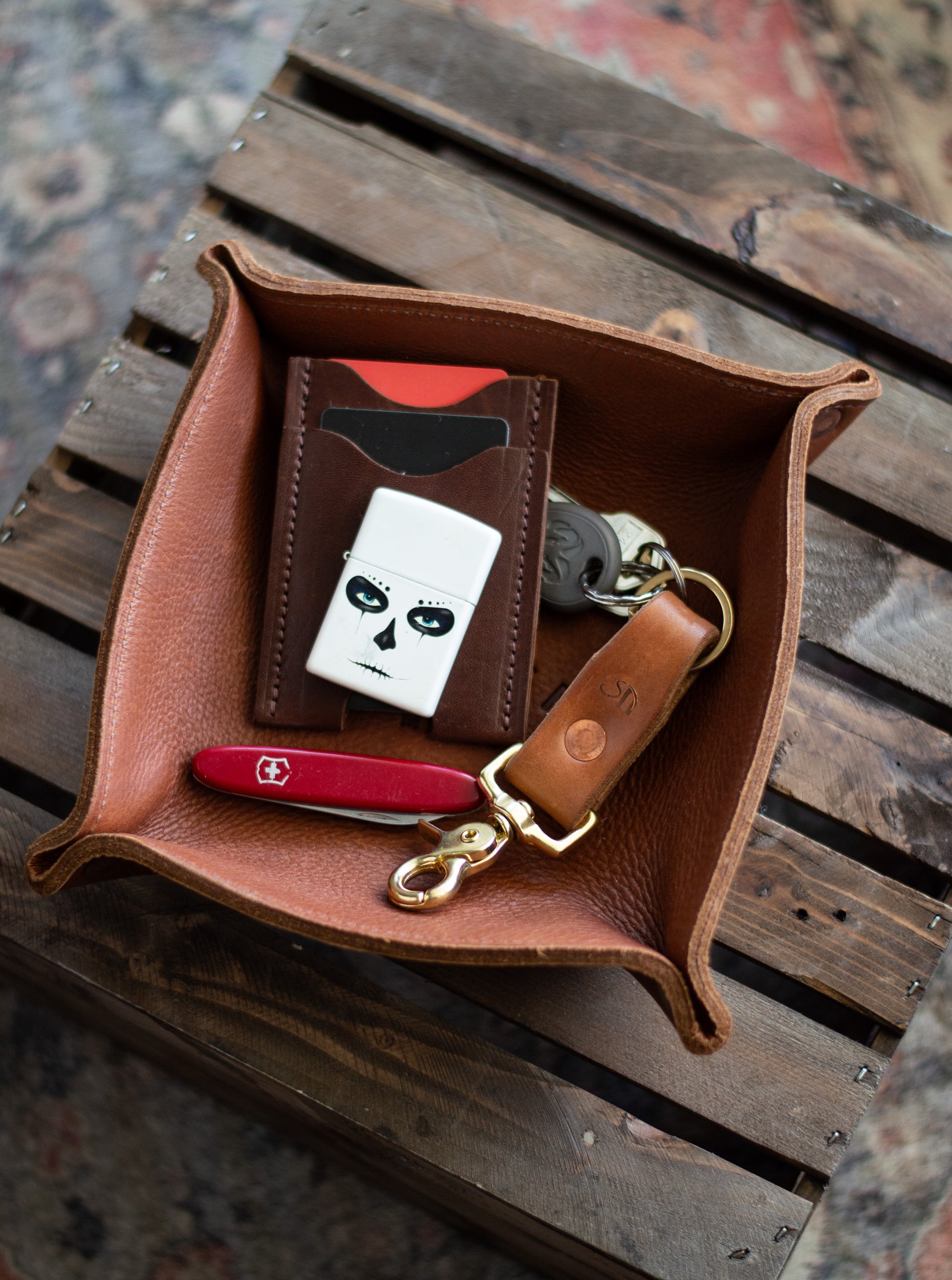 A leather valet tray is filled with various mens items, including a wallet, pocket knife & keys.