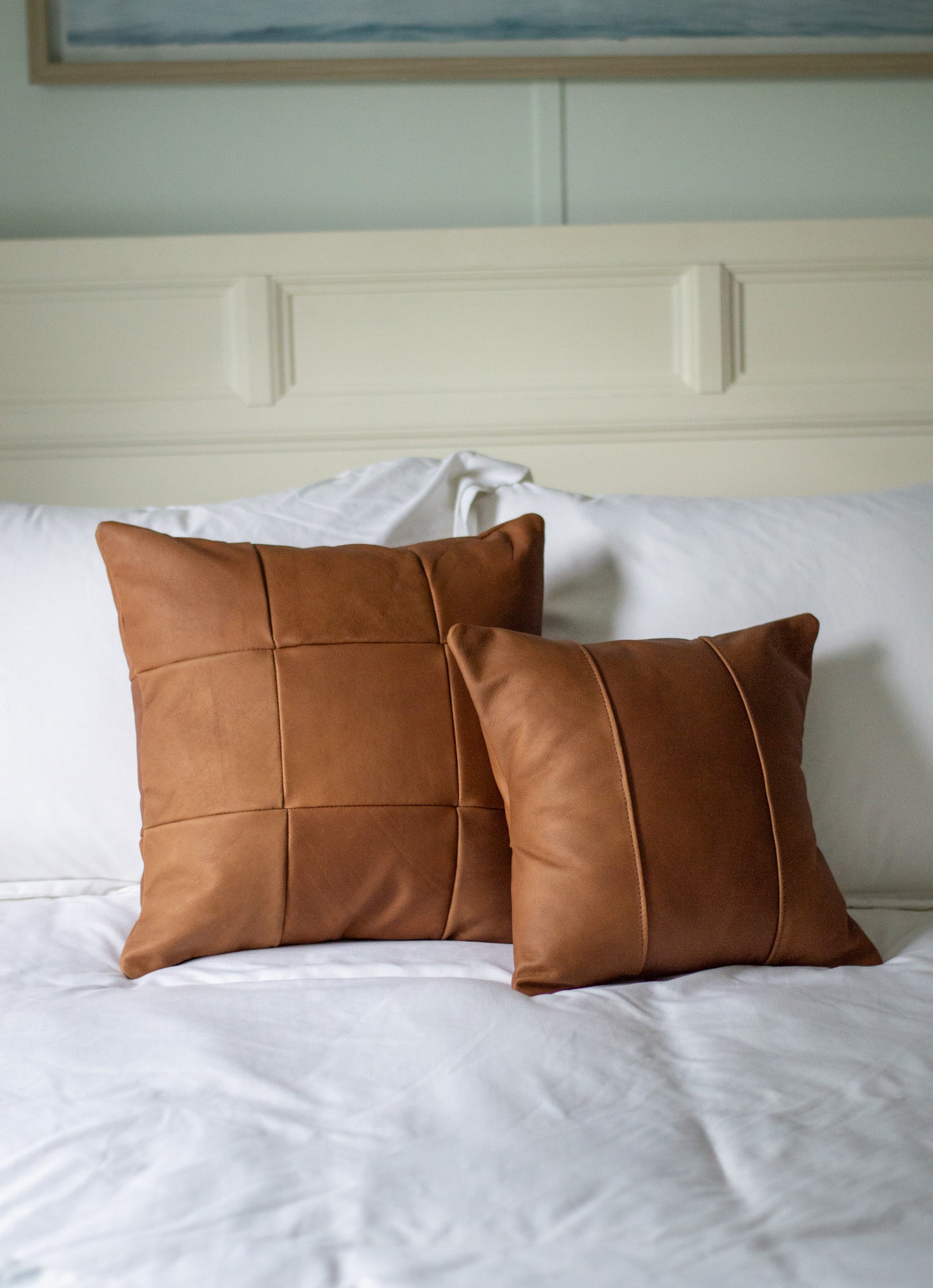 A set of the small & large Leather Pillows sits on a bed.