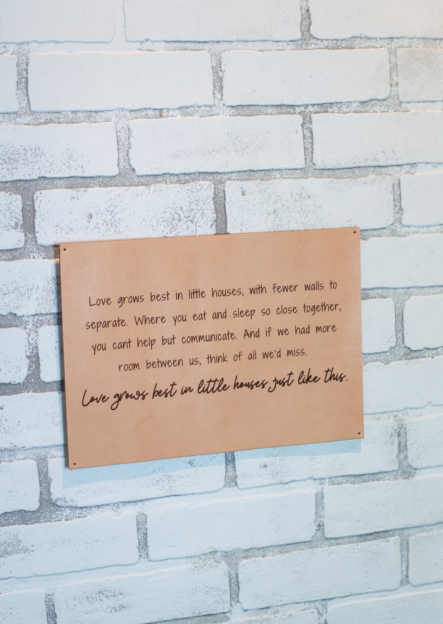 The Urban Southern handcrafted leather "Love Grows Best" sign hangs on a brick wall.