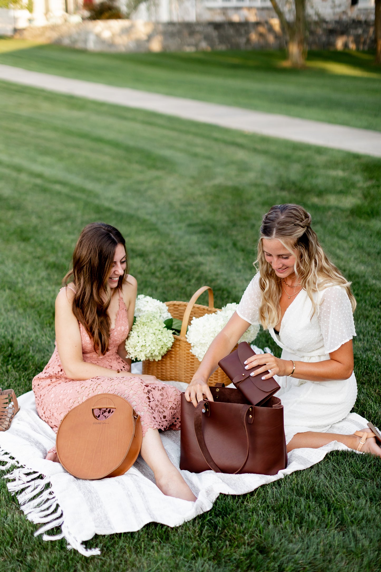 One woman pulls an Urban Southern 5th Avenue Clutch Wallet from her Urban Tote while sitting next to a woman using the Urban Southern Britt Circle Crossbody.