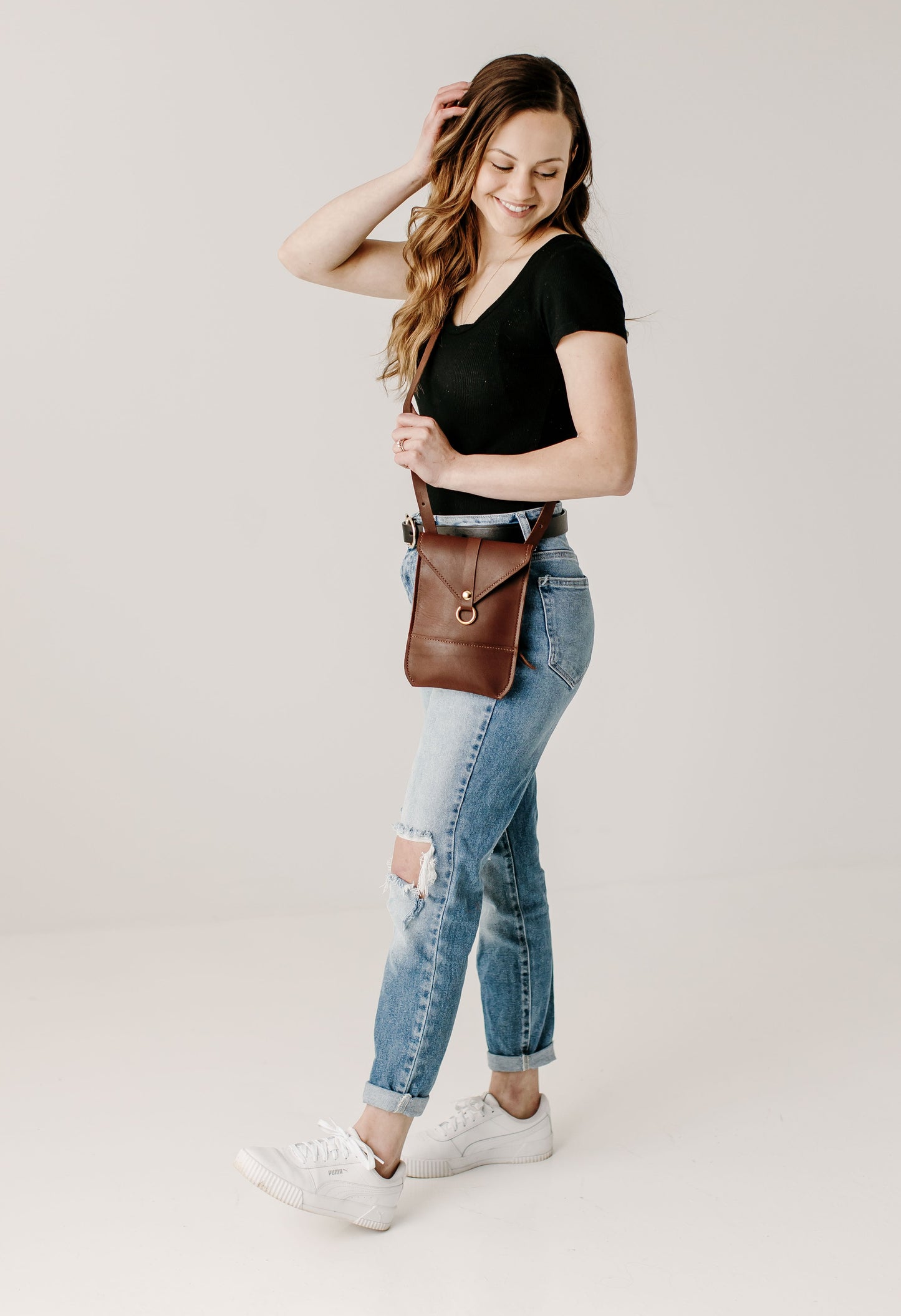 A woman wears a chestnut Postal Crossbody across her body.