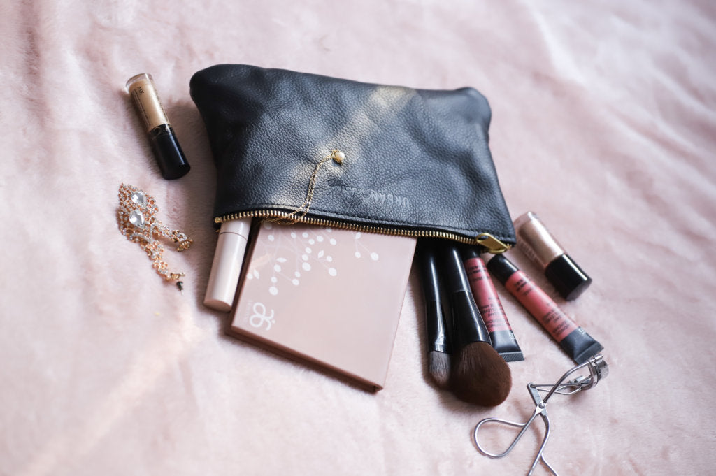 Makeup pours out of a Zipper Pouch, shown in Black.