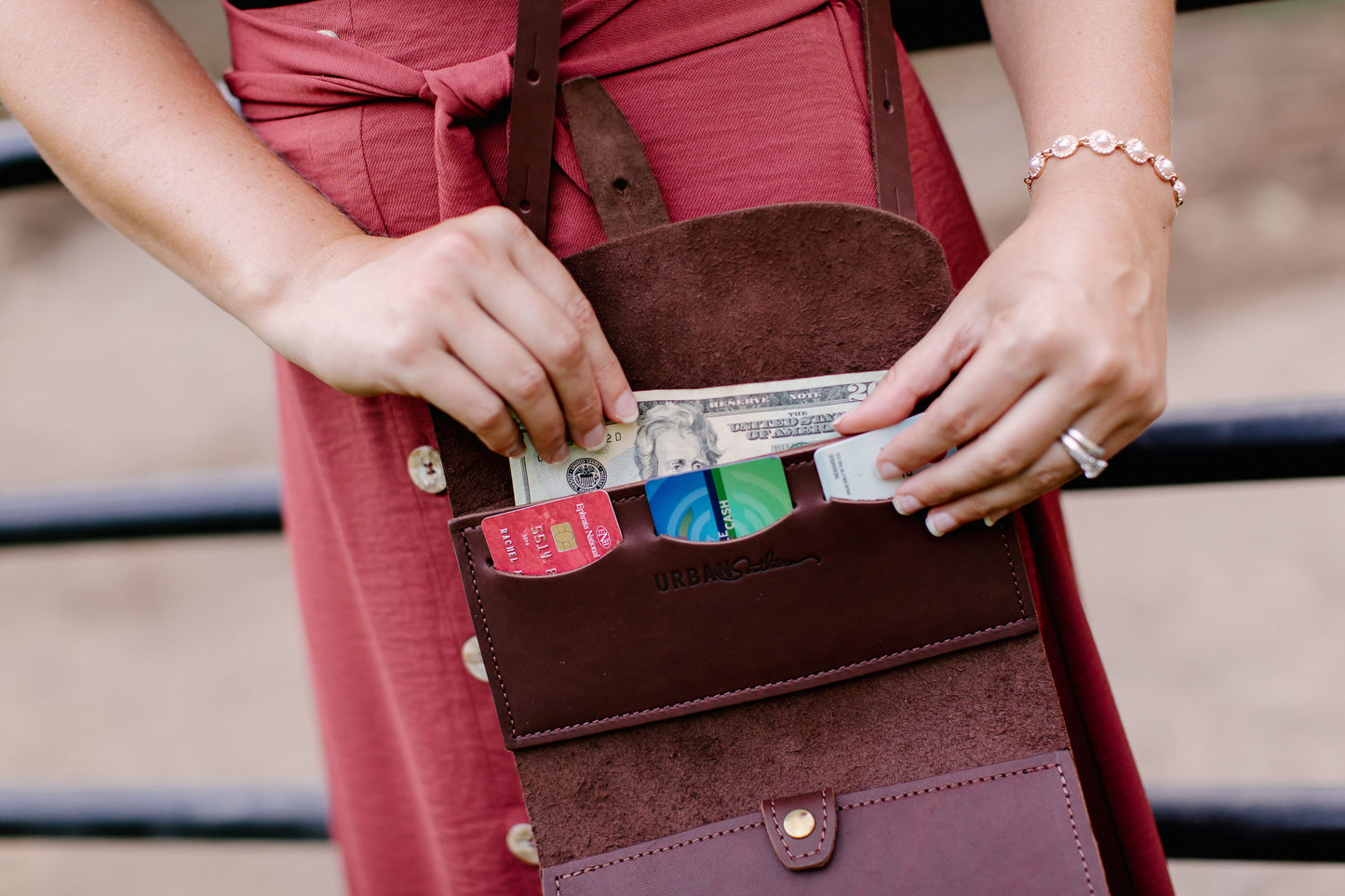 A woman pulls cash from the upper cash pocket on the Crossbody Wallet in Chestnut Brown.