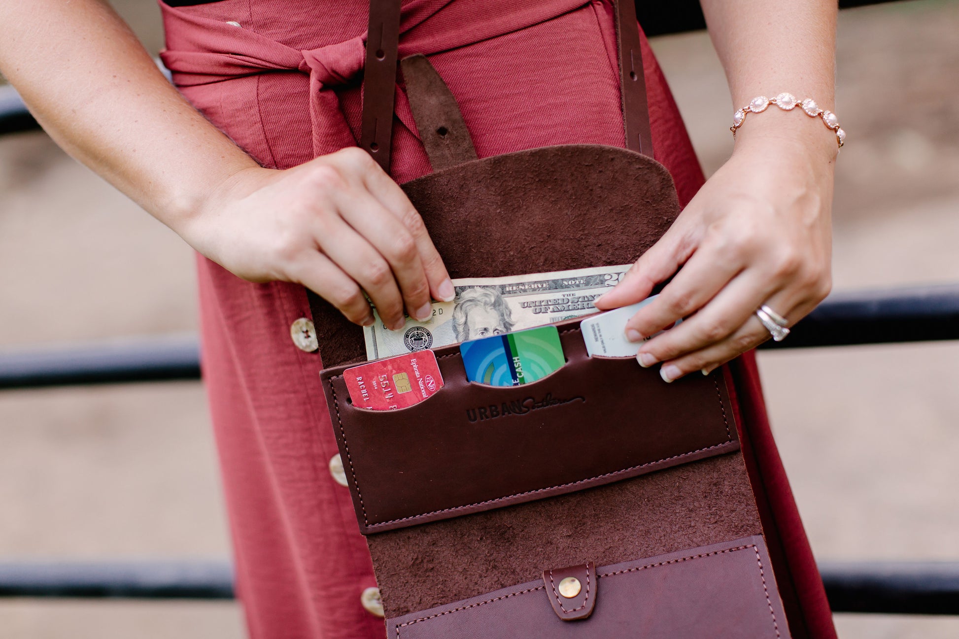 A woman pulls cash from the upper cash pocket on the Crossbody Wallet in Chestnut Brown.